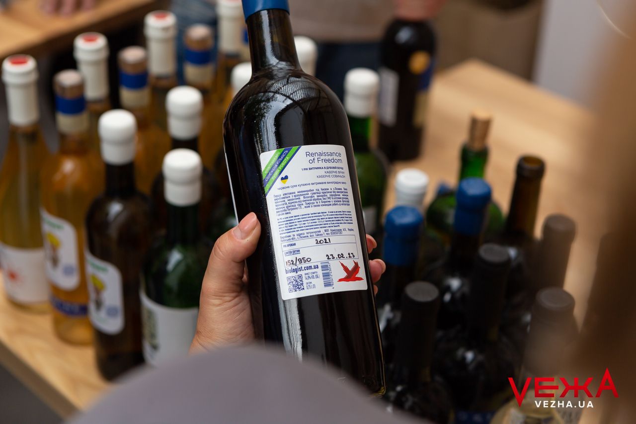 Hand holding wine bottle showing back label against background of other bottles.