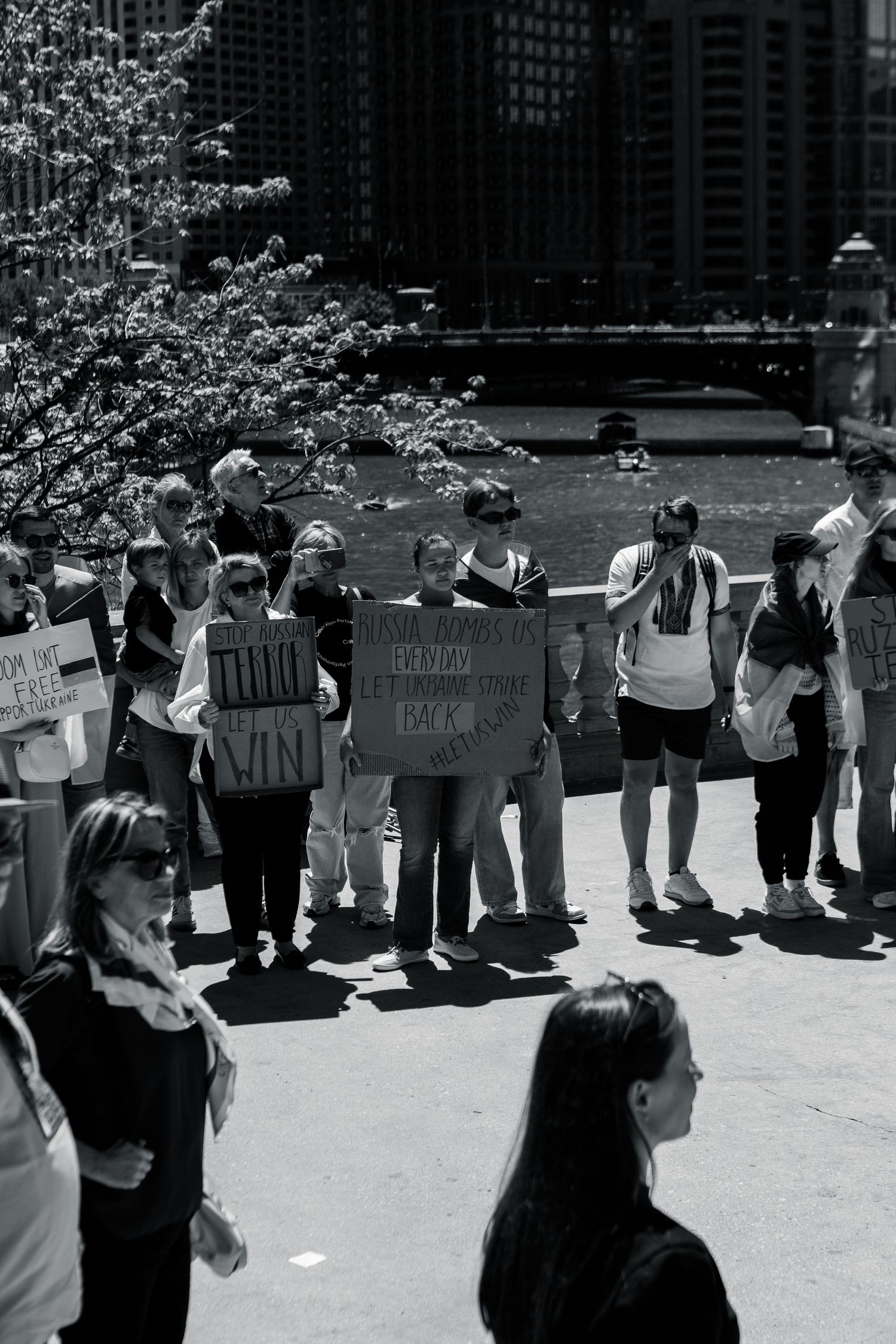 Group of protesters gathered outdoors holding signs in black and white cityscape.