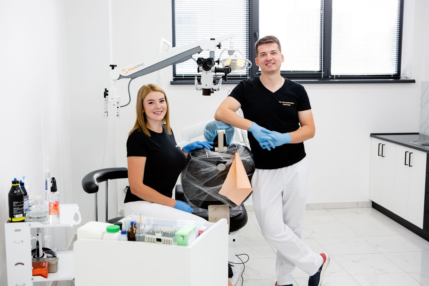 Dental professionals in black uniforms working together in a modern clinic treatment room.