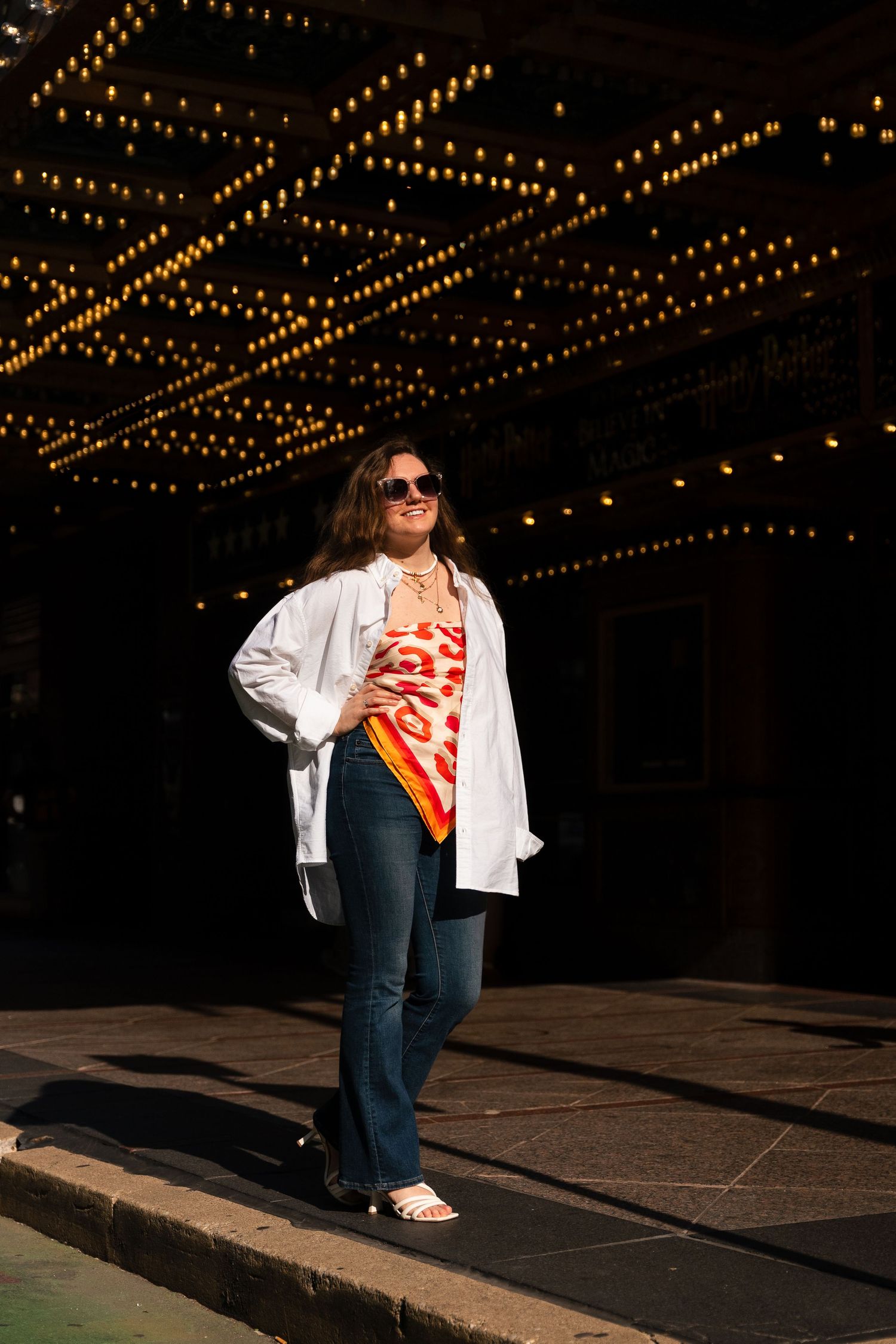 Street fashion shot under decorative ceiling lights wearing white shirt and jeans.