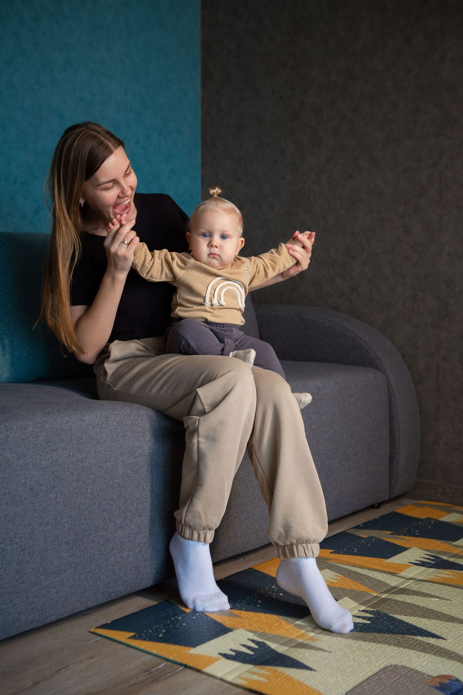 A sequence of five photos showing playful interaction between an adult and baby on a gray couch with a patterned rug below.