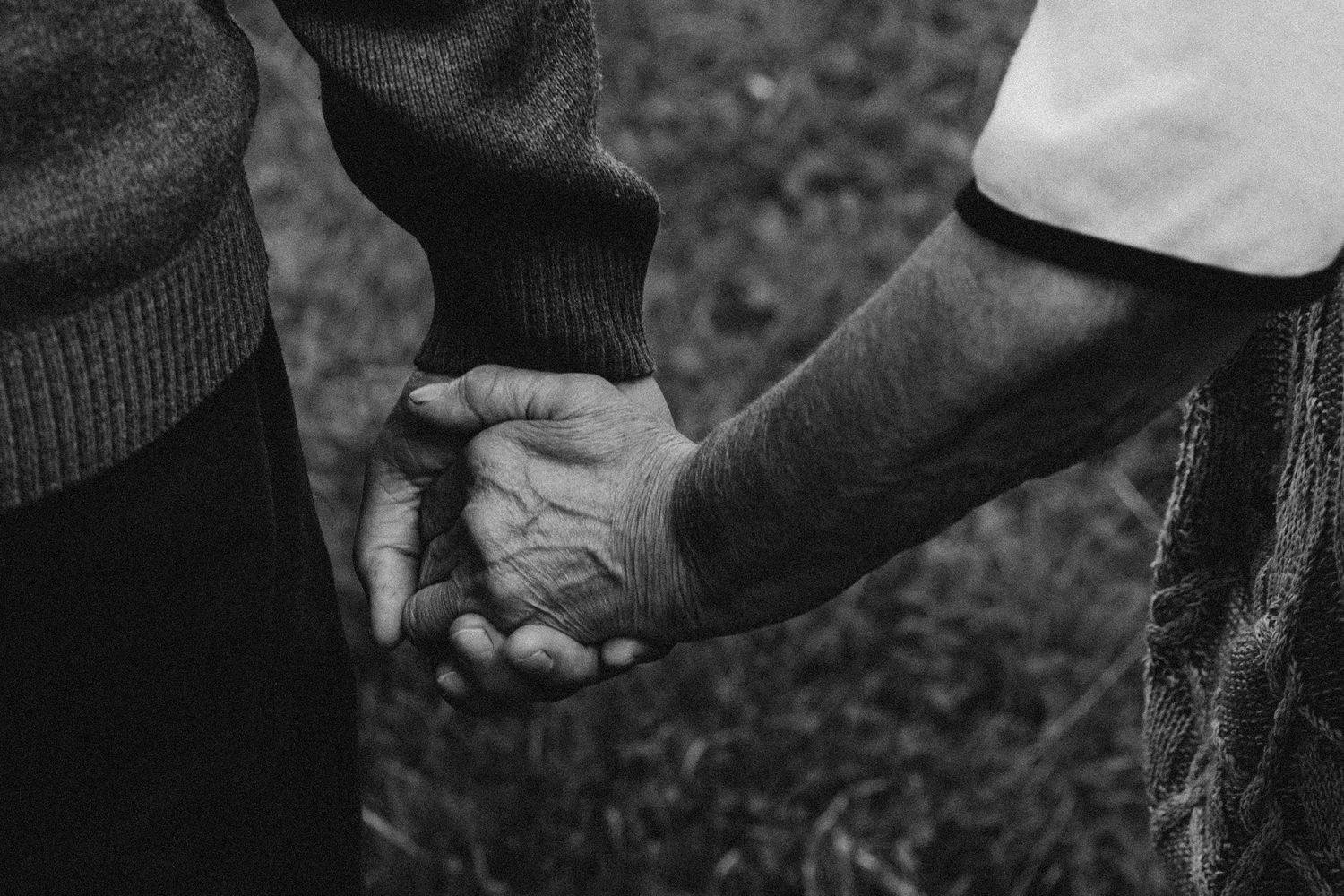 A black and white close-up shot of two hands clasped together outdoors.