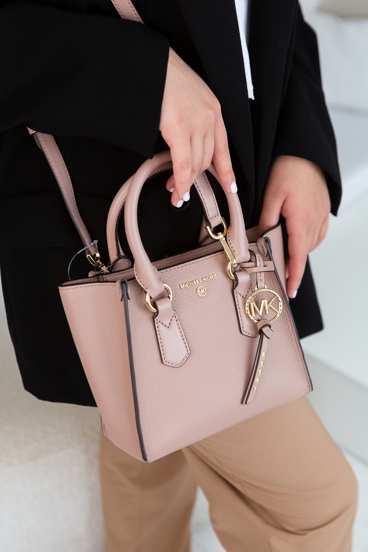 Blush pink Michael Kors mini satchel bag with gold hardware and charm displayed against black clothing.
