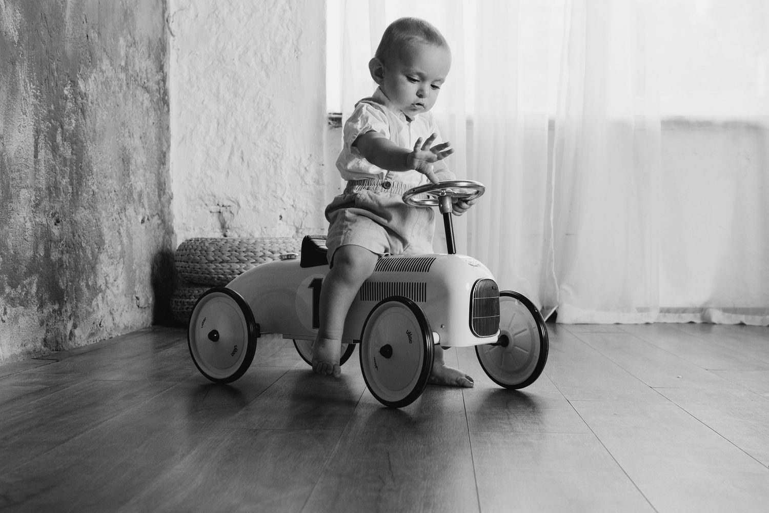 A black and white photo of a child sitting in a vintage metal pedal car.
