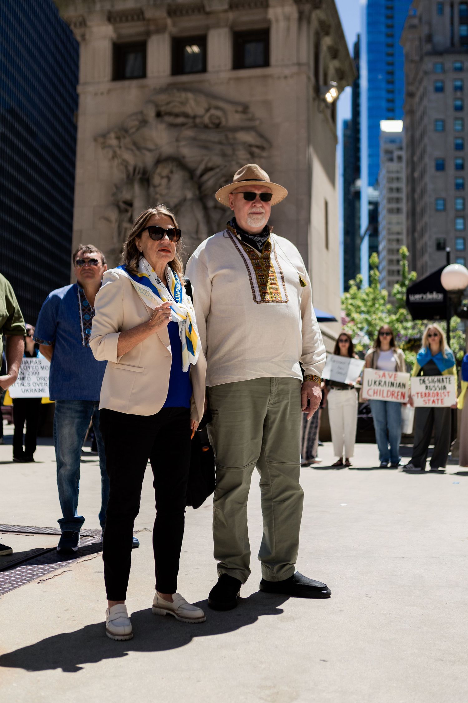 Protesters gather on a sunny day in downtown Chicago holding signs and flags.