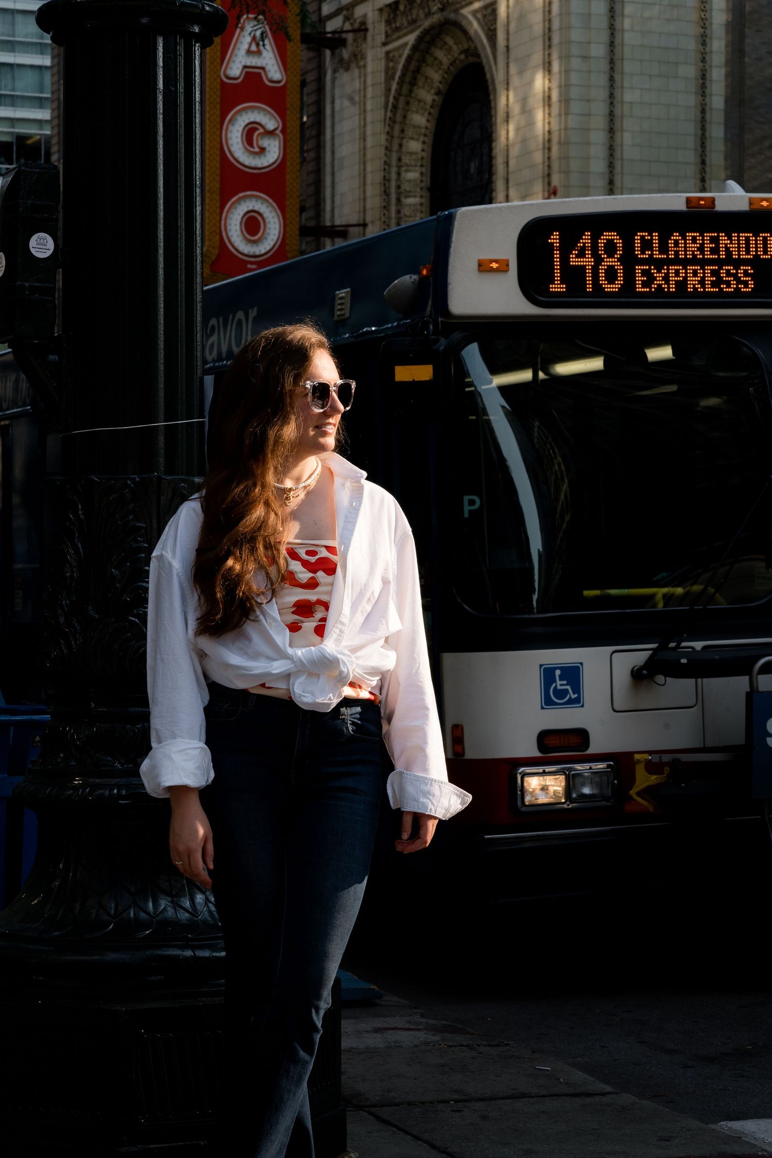 A person in a white top and sunglasses stands near a city bus with 149 Claremont Express displayed on its sign.