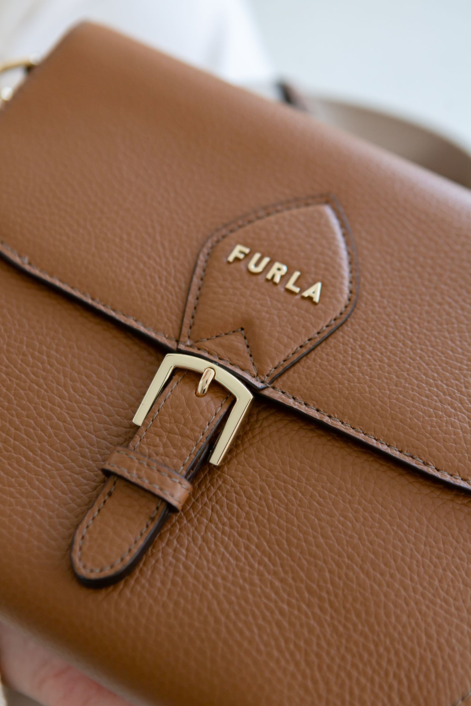 Brown leather Furla bag with gold buckle detail in close-up view.