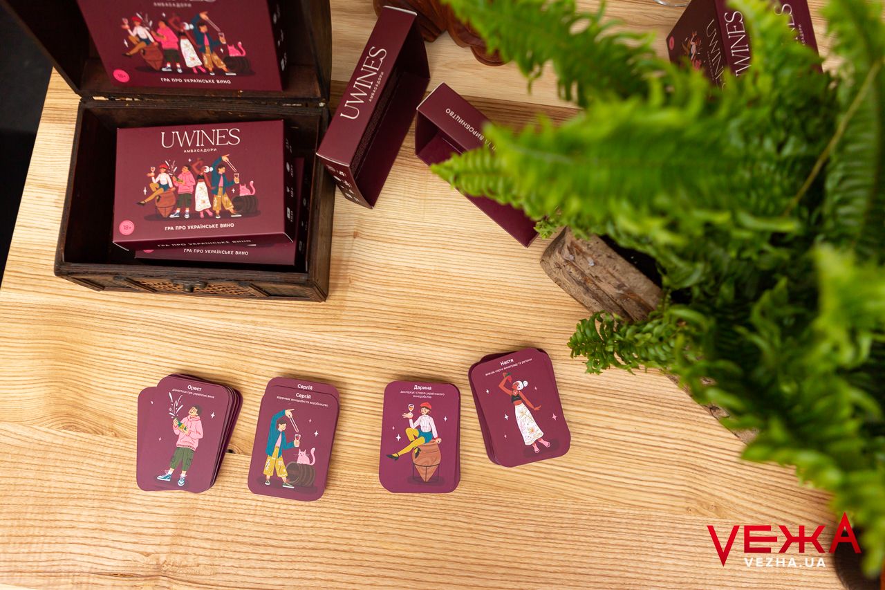Wine-themed decorative cards displayed on wooden surface next to green plant.