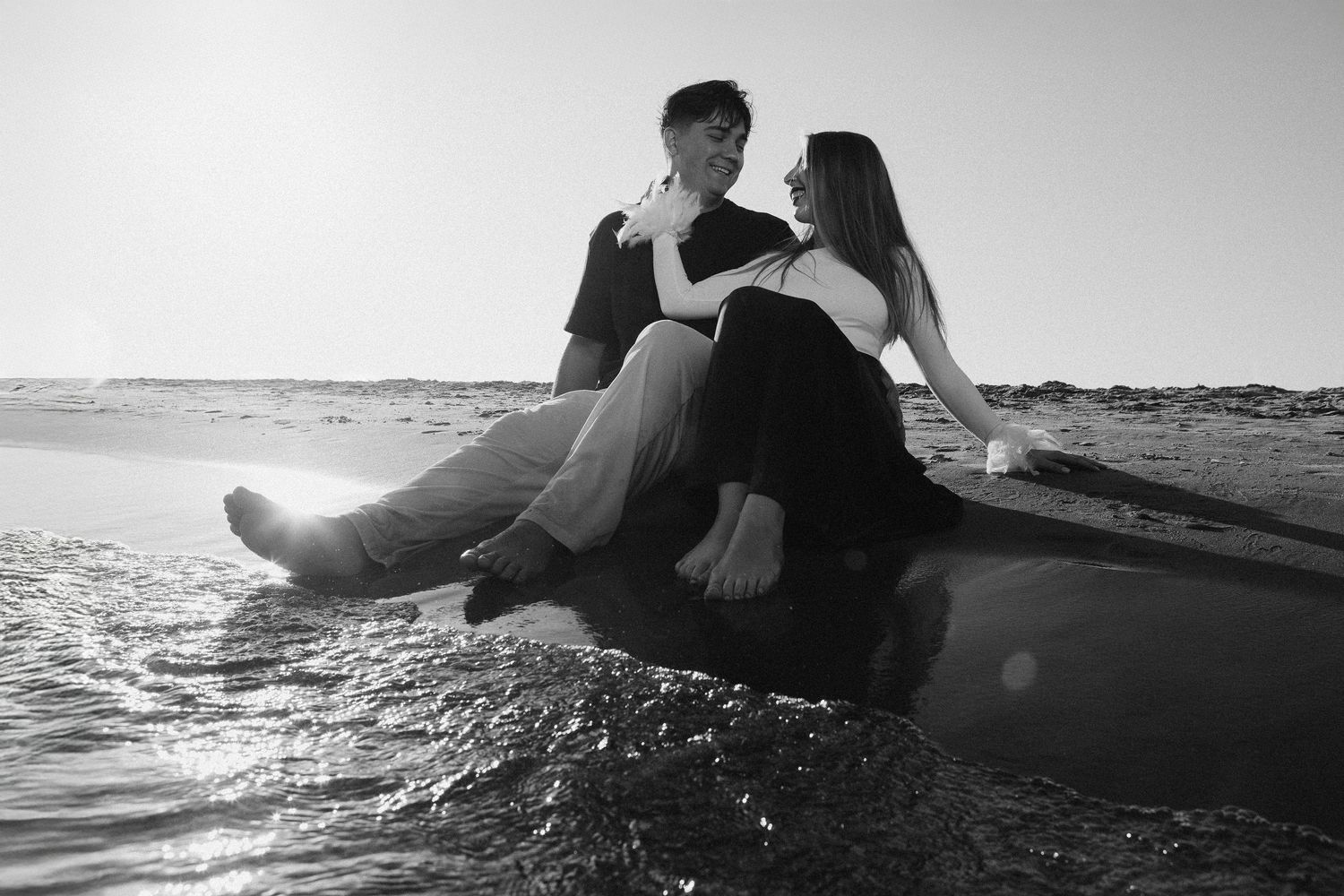 A series of romantic black and white photos showing a couple embracing on a beach at sunset.
