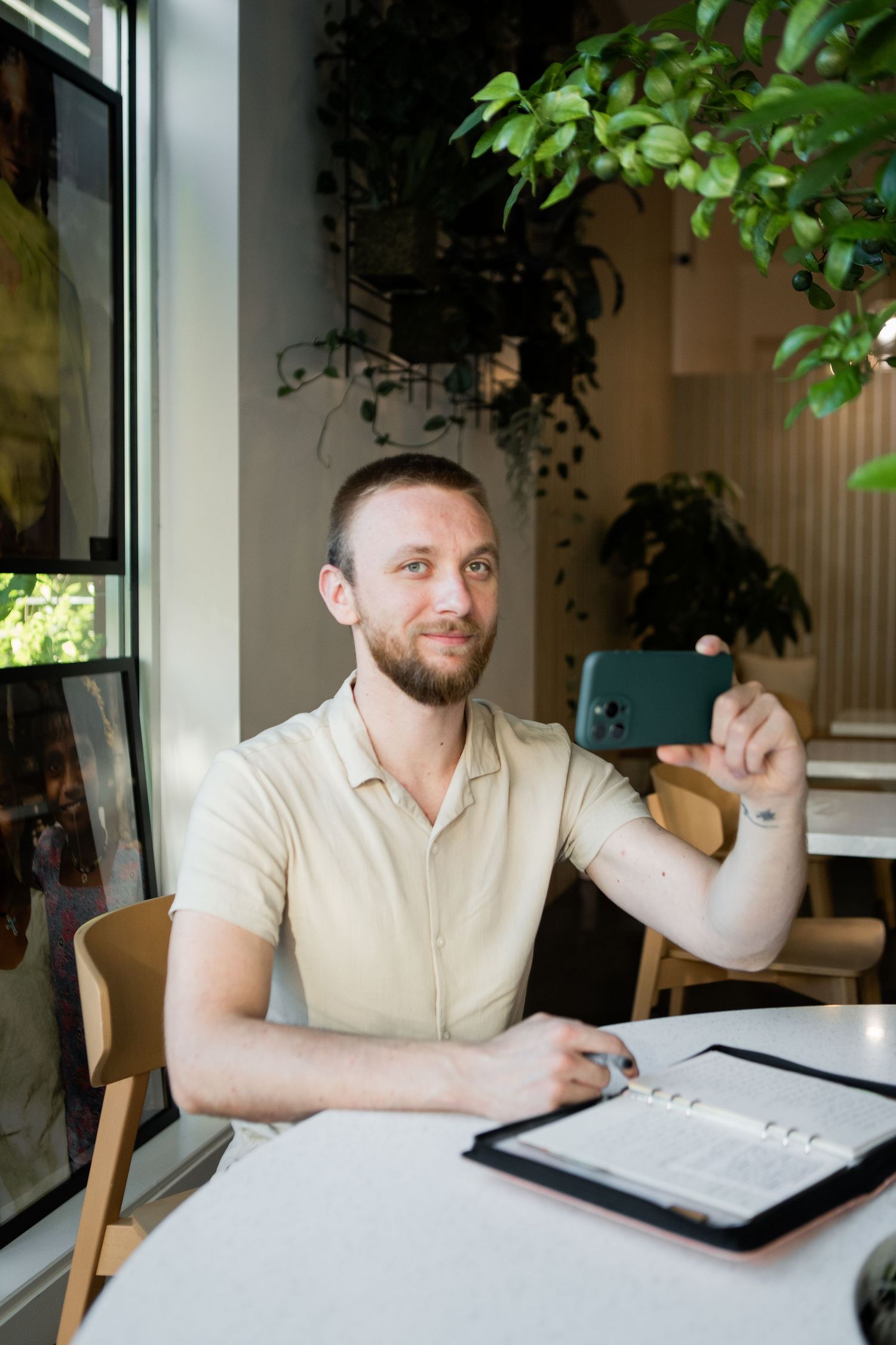 Professional working on digital tablet in bright cafe setting with houseplants in background.