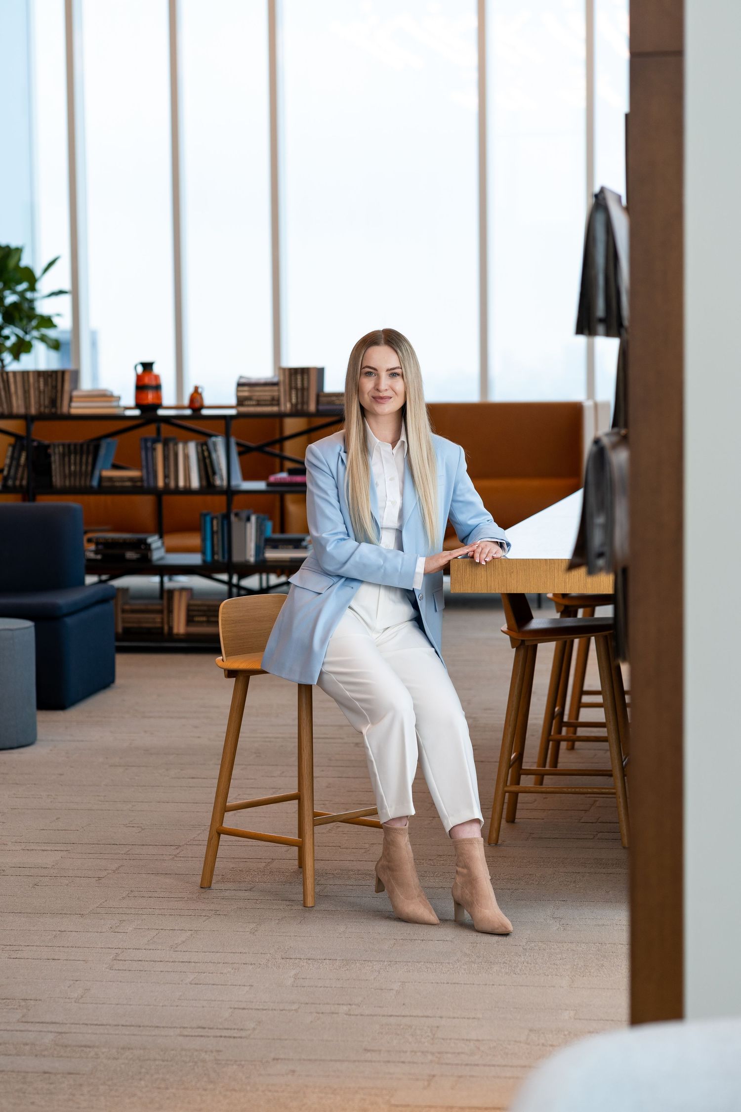 Business professional in blue blazer sits on barstool in modern office space.