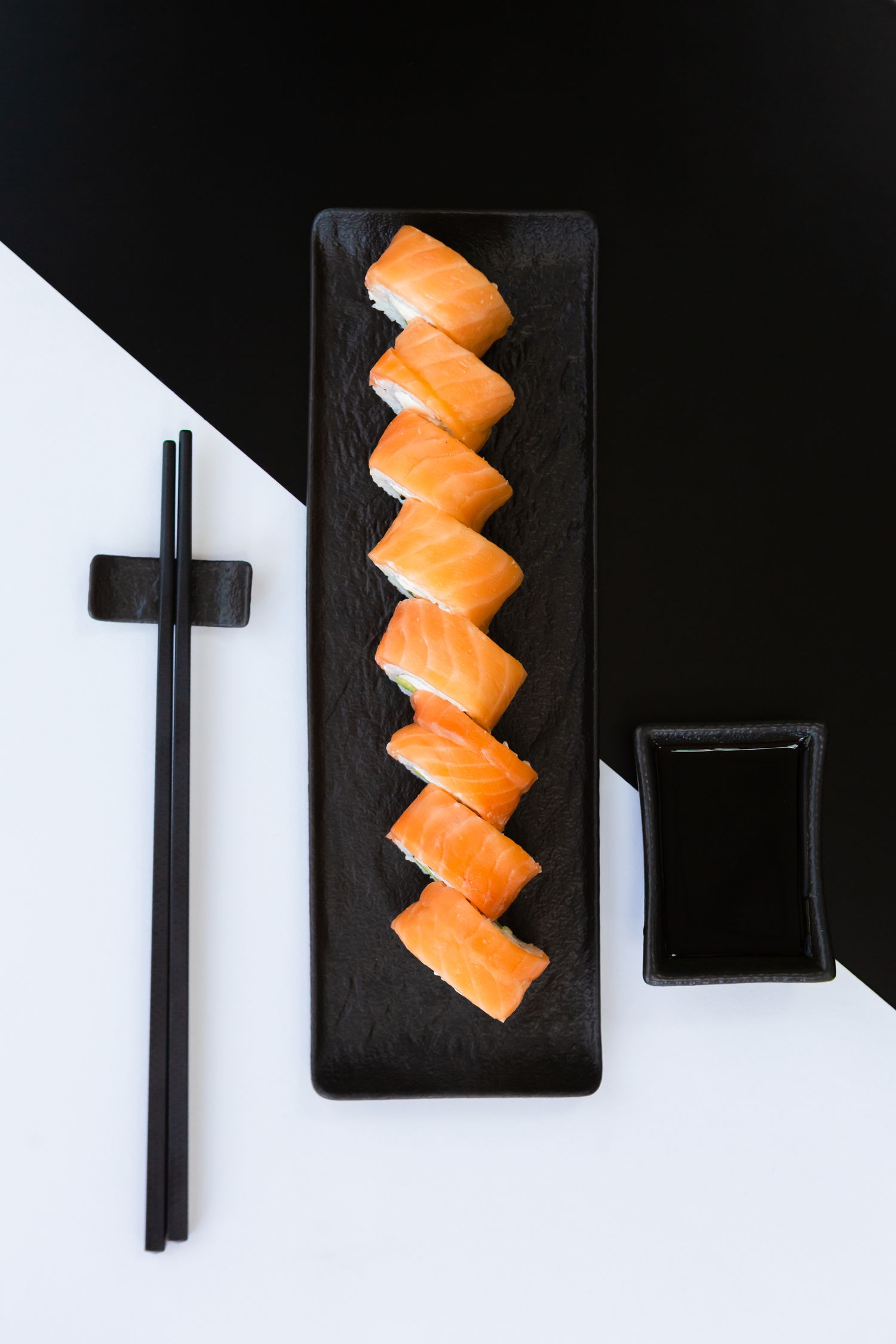 Eight pieces of salmon sushi arranged on black plate with chopsticks and soy sauce.