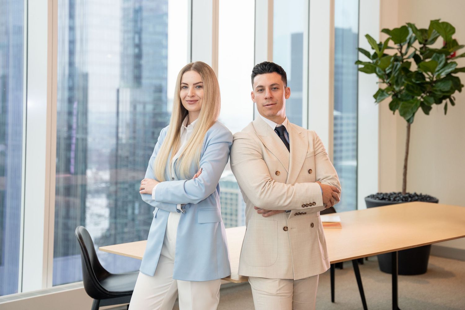 Business partners in coordinating suits stand confidently in modern office setting.