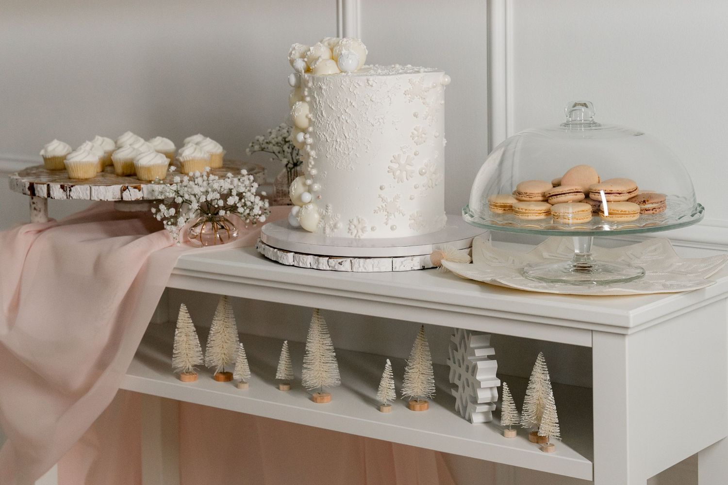 Elegant dessert table display with white cake, macarons and winter decorations.