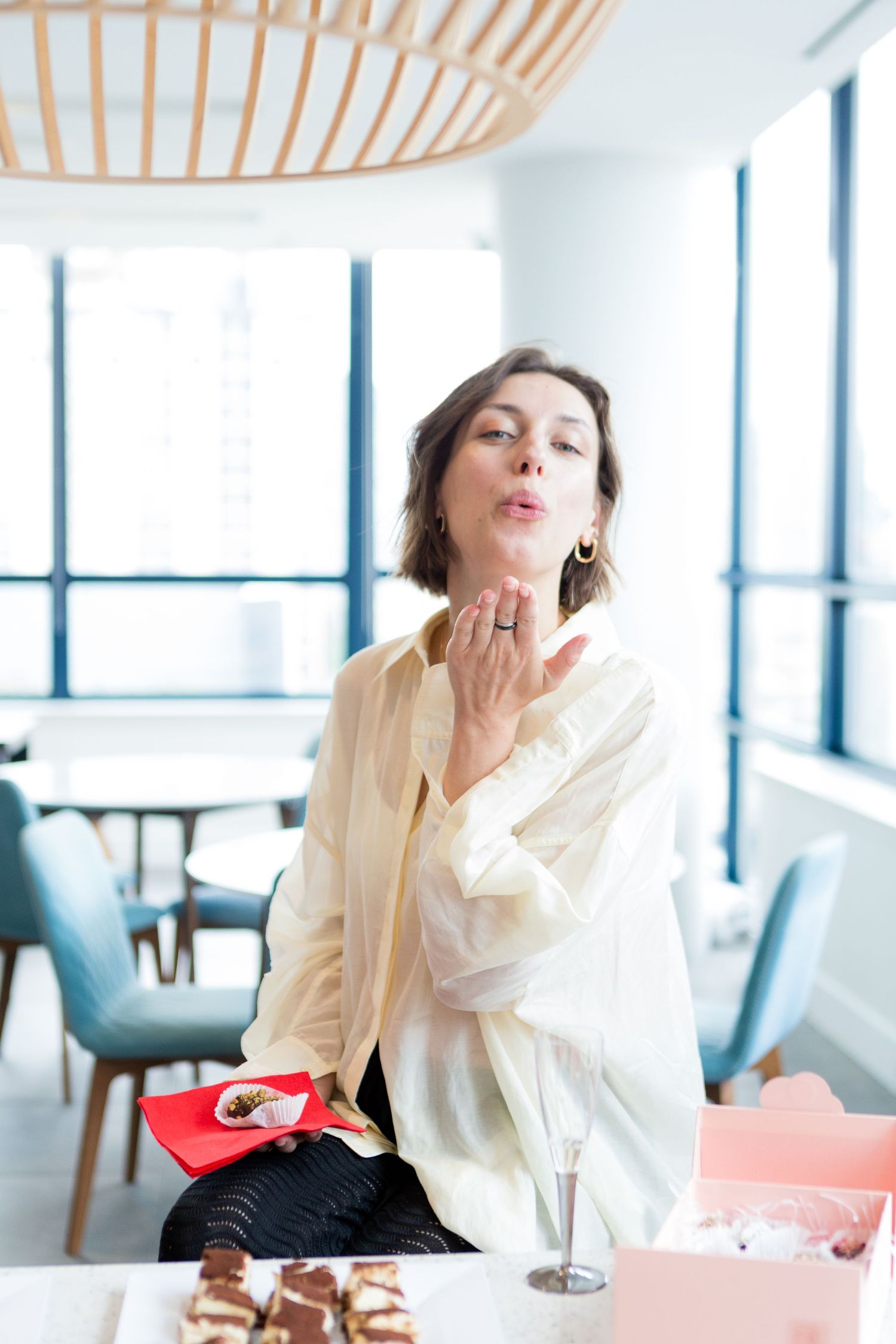 Woman in white blowing kiss while sitting at table with desserts in modern space.