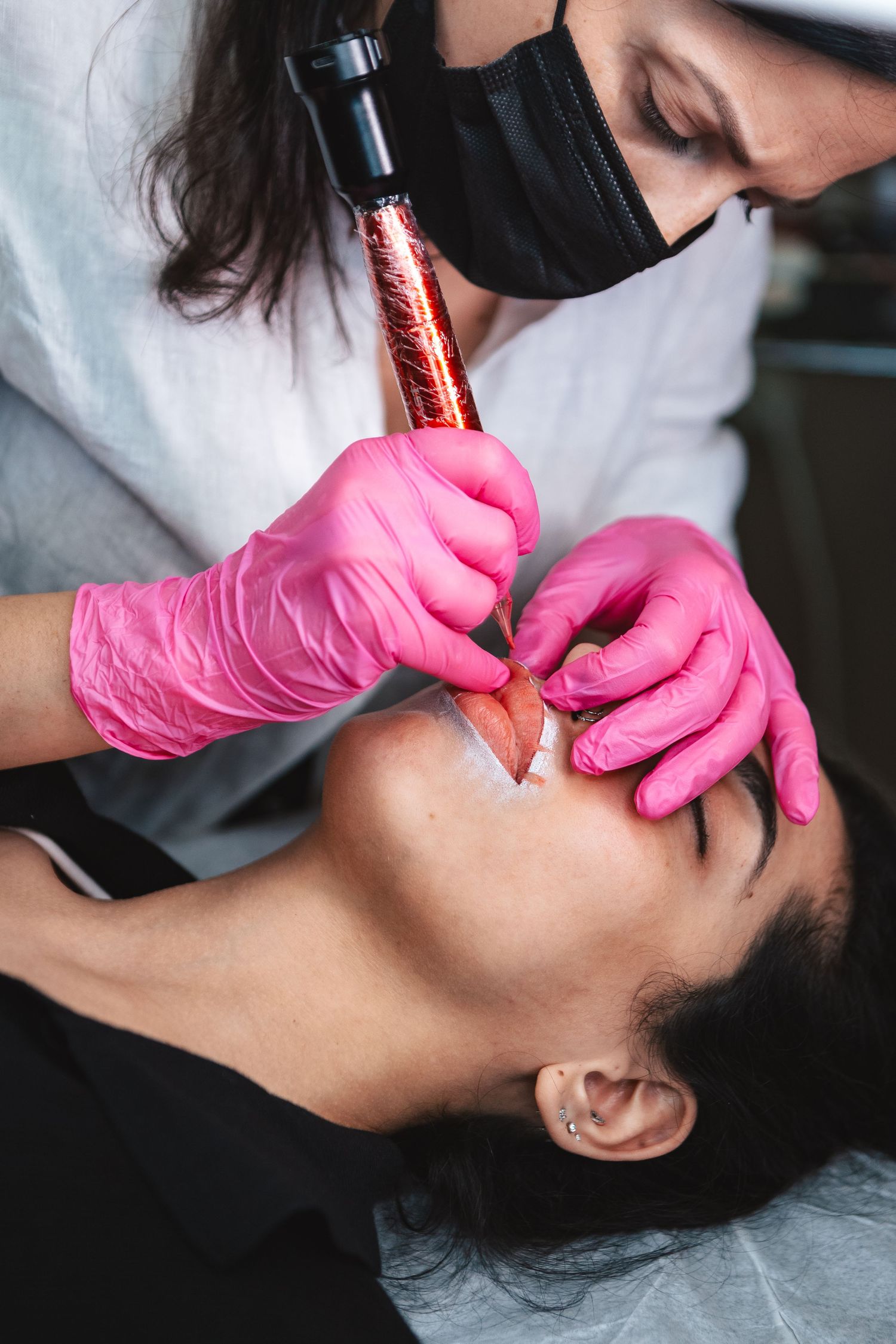 A cosmetic technician performing permanent makeup application wearing protective gear.