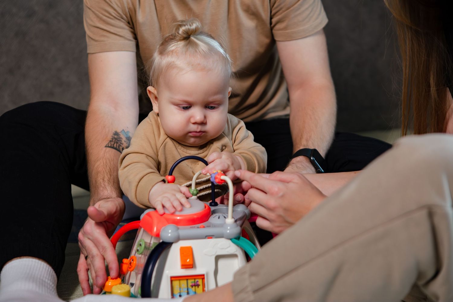 A baby plays with colorful educational toys while sitting at a table with adult guidance.