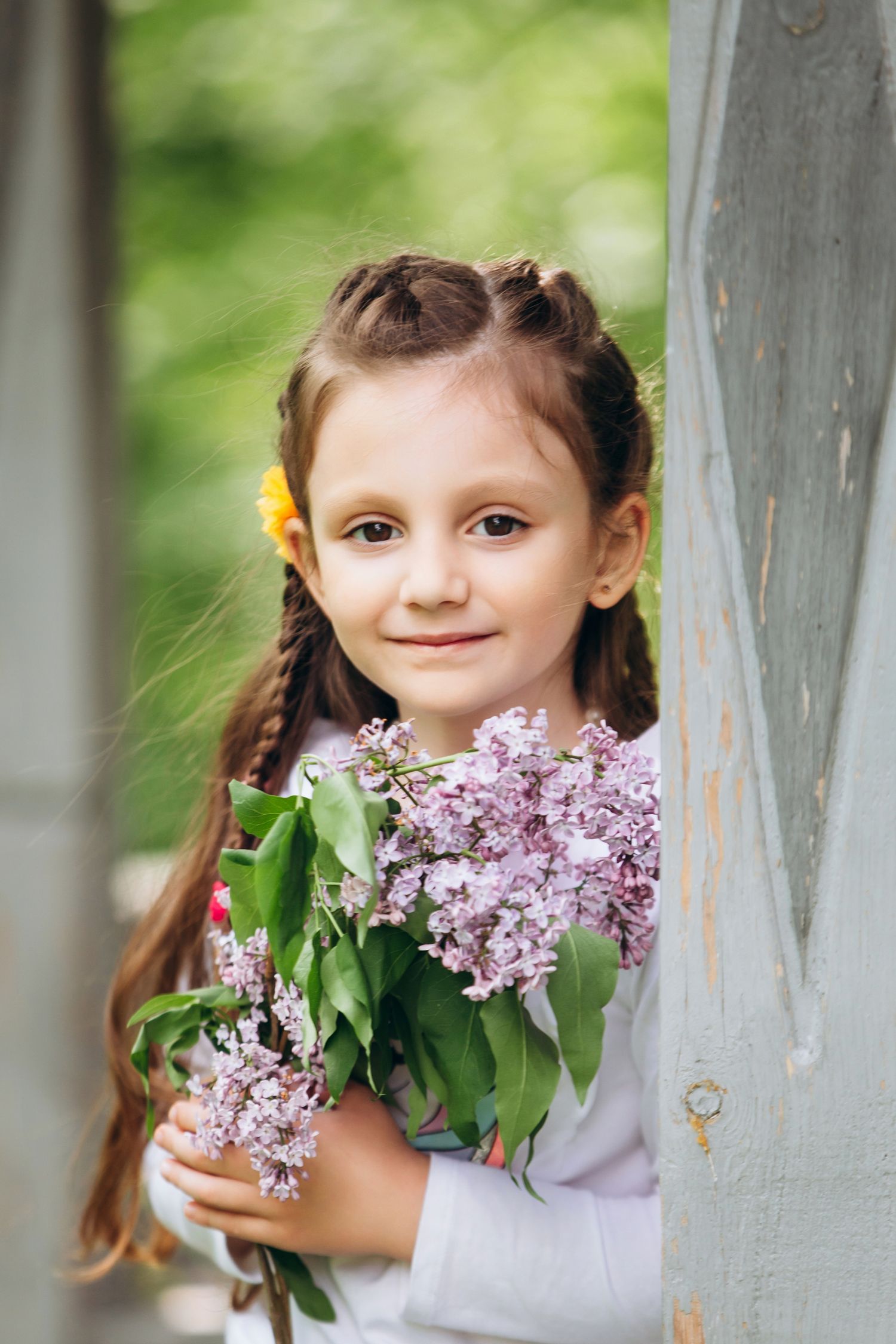 A child holding fresh lilac flowers against a rustic background.