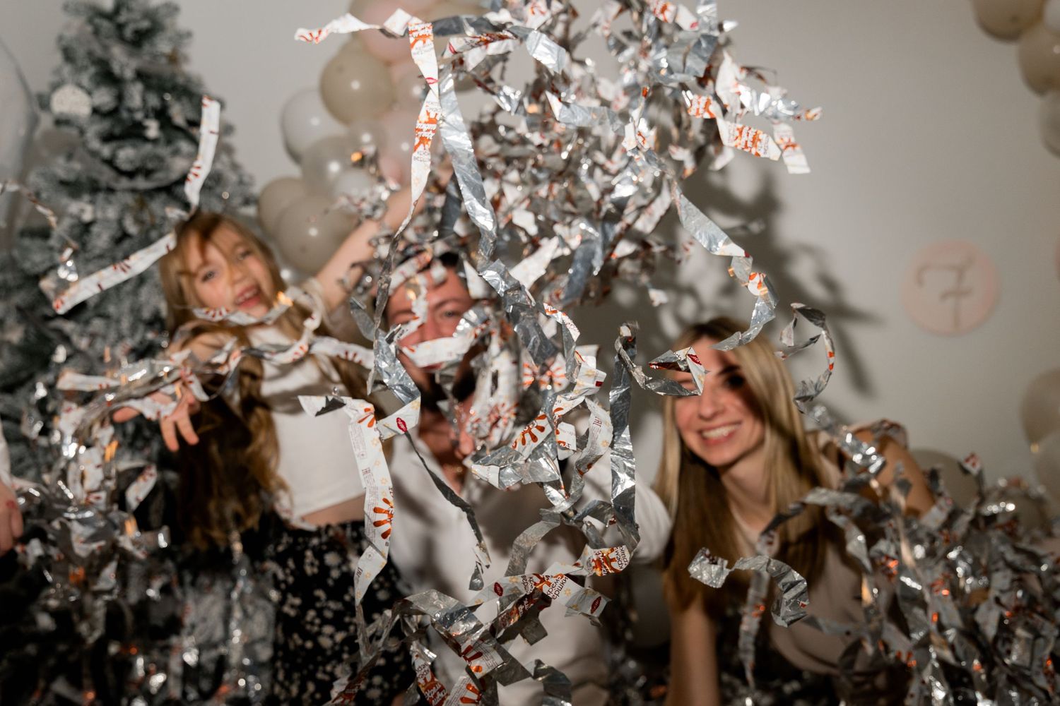 Fun party scene with multiple people throwing silver confetti near Christmas decorations.