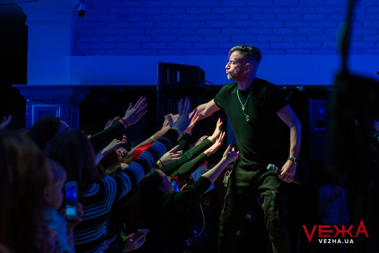 A performer engages with an enthusiastic crowd during a concert with blue stage lighting.