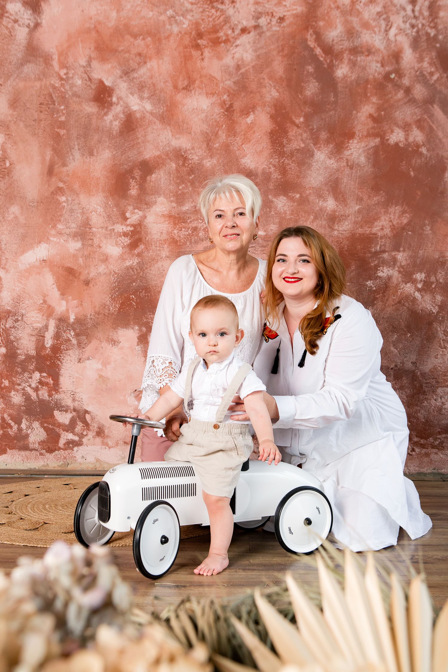 A heartwarming family portrait with a vintage white pedal car against a textured coral backdrop.