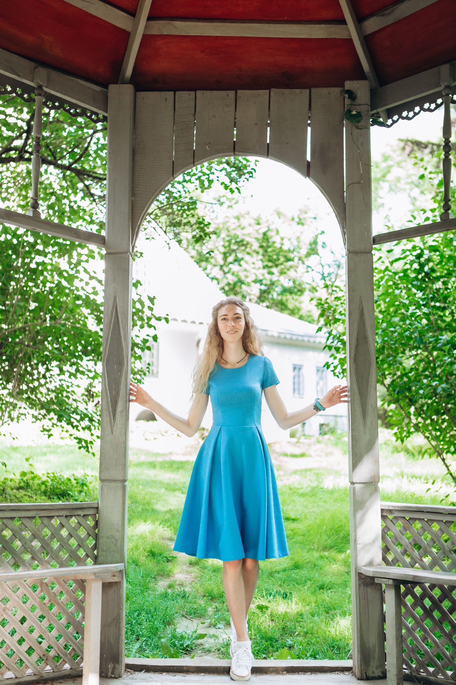 Bright summer scene with blue dress in white gazebo surrounded by greenery.