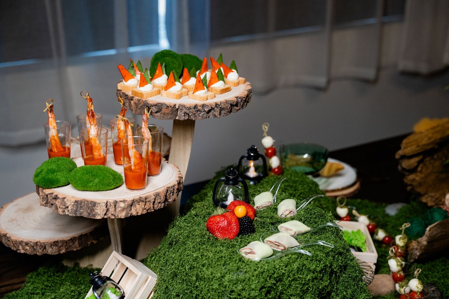 Elegant catering display with tiered appetizers and decorative greenery on rustic wood platforms.