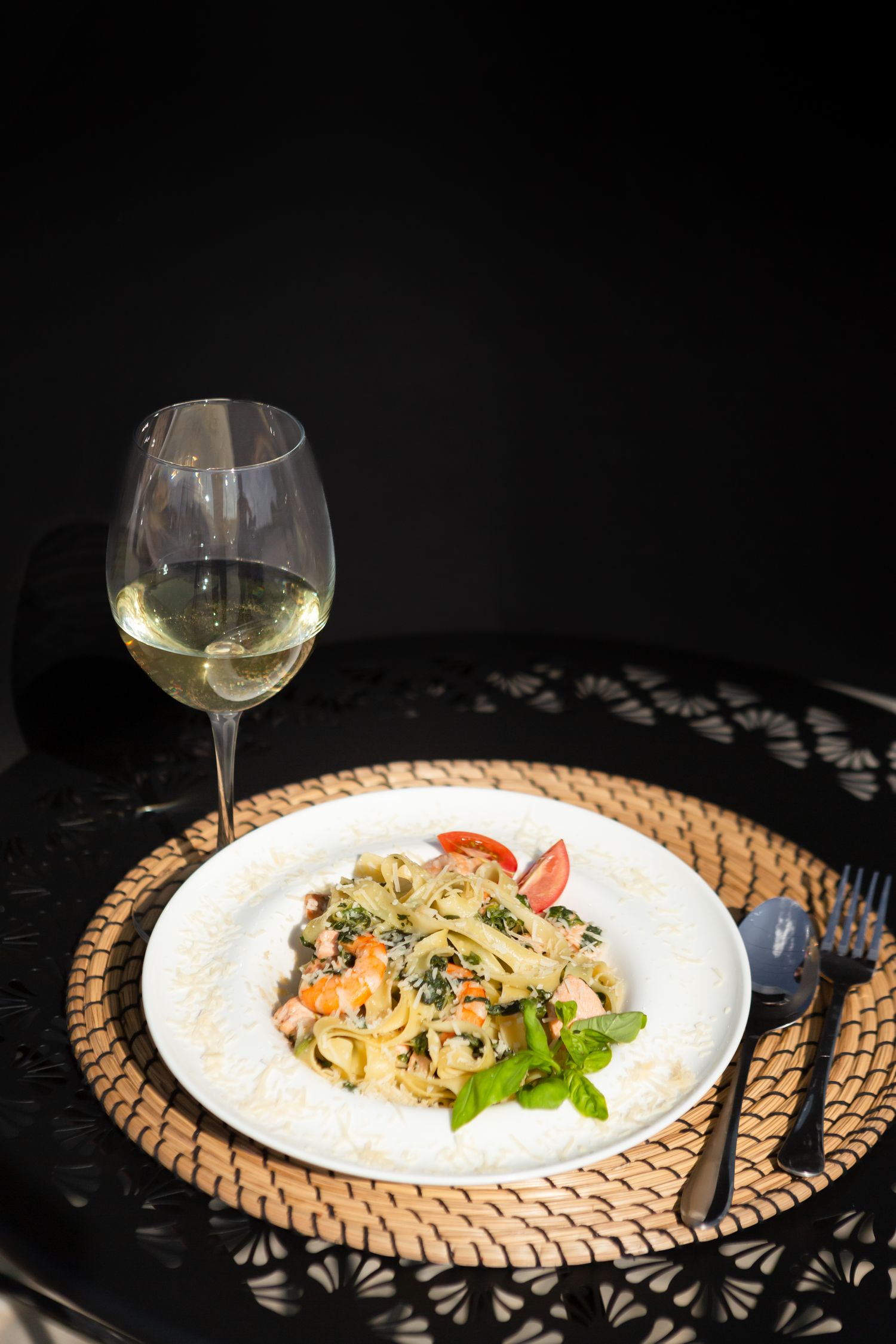 Pasta dish served with white wine on woven placemat against dark background.