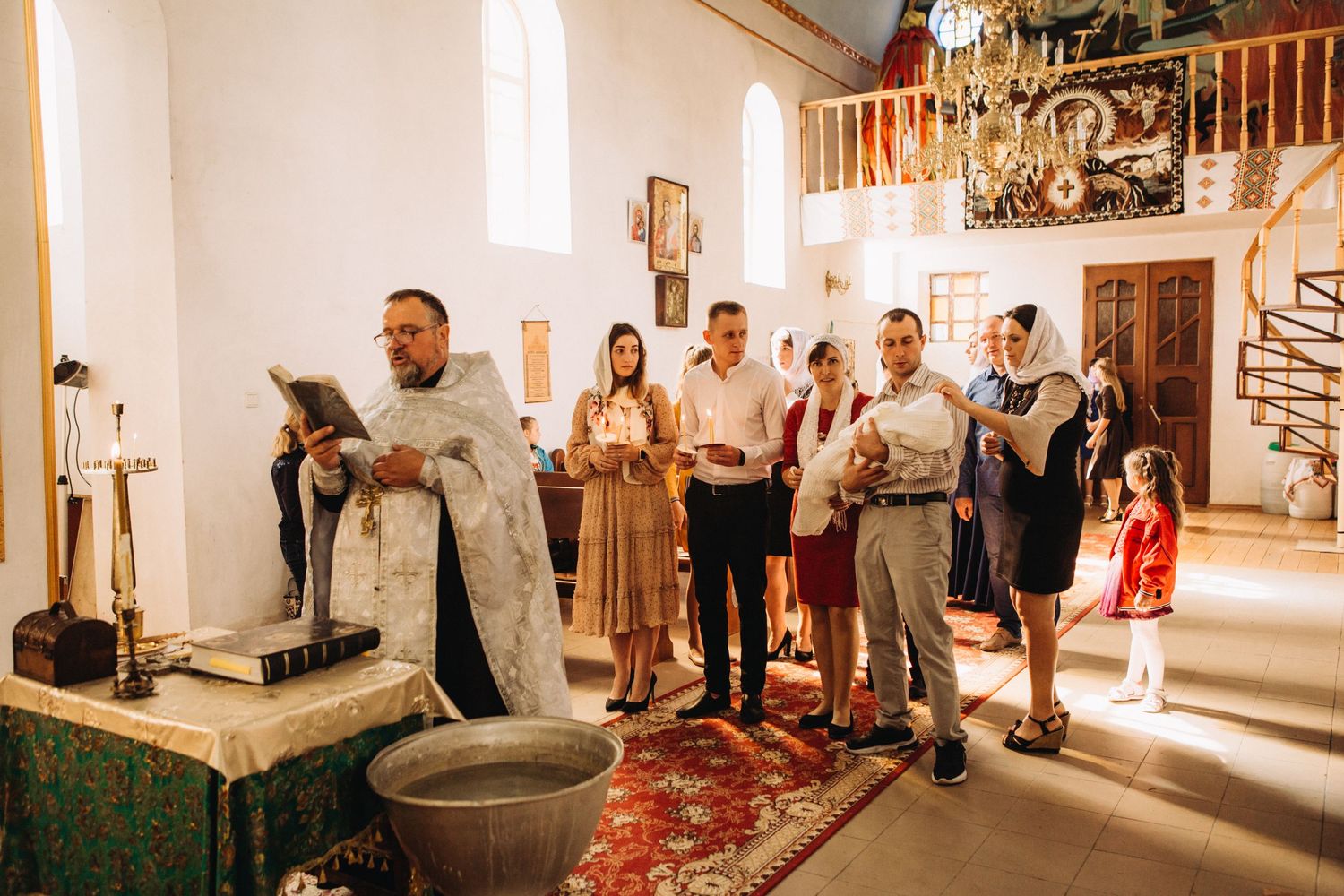 Church interior during Orthodox ceremony with congregation standing near baptismal font.