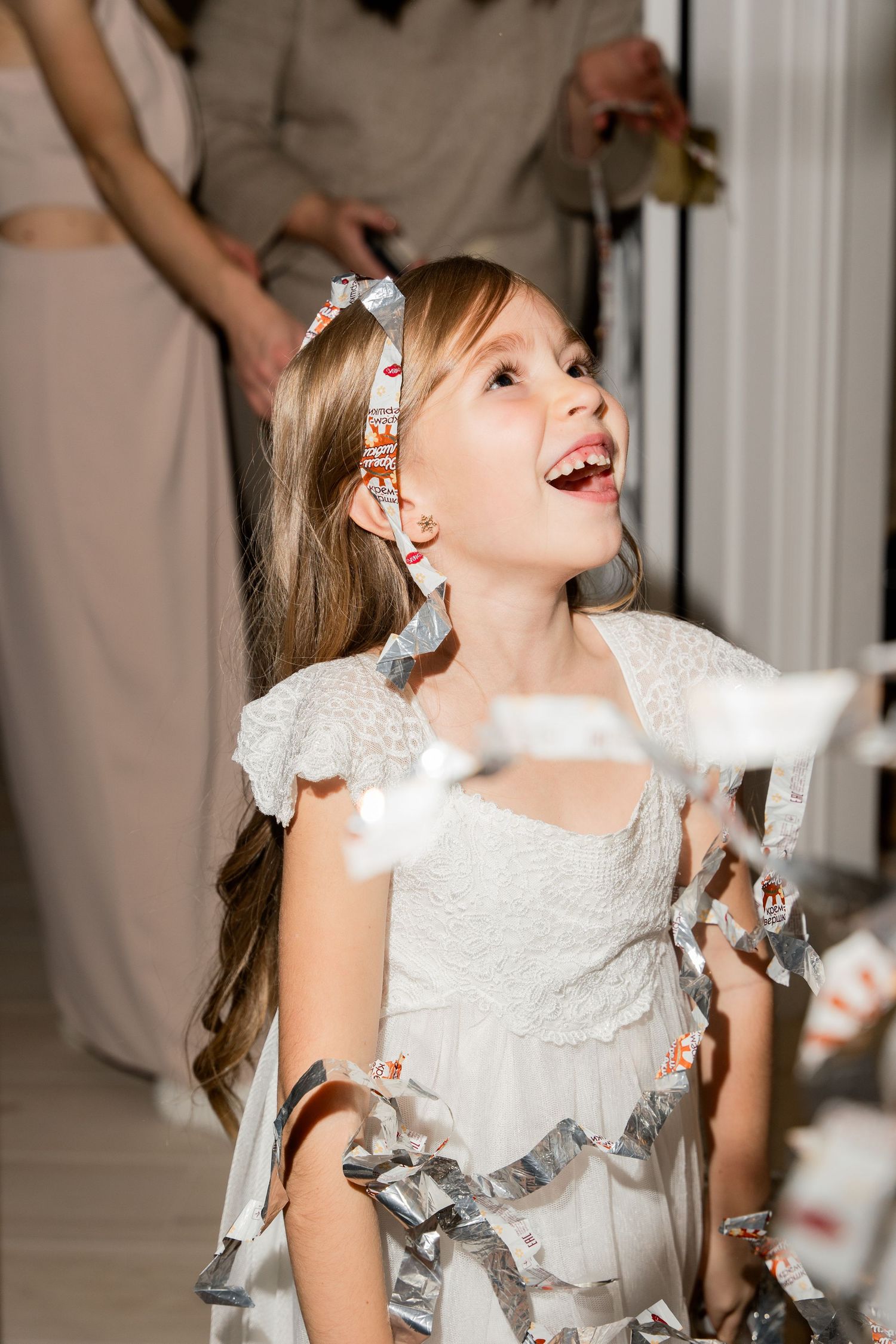Young party guest in white dress playing with silver streamers during celebration.