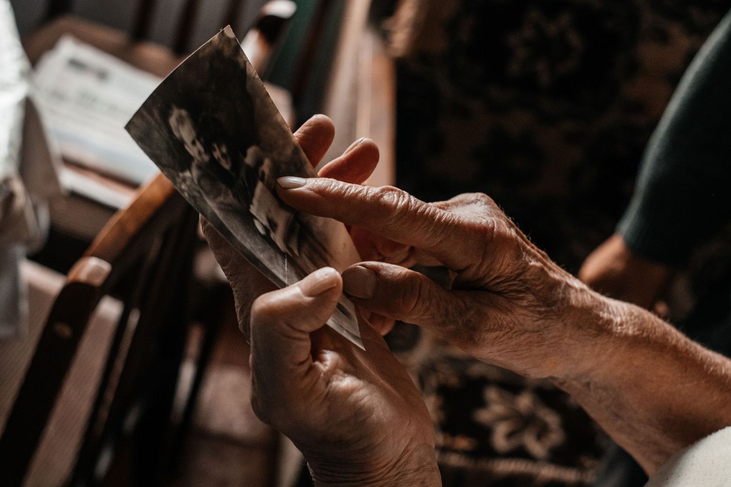 Weathered hands holding and examining old photographs in dim lighting.