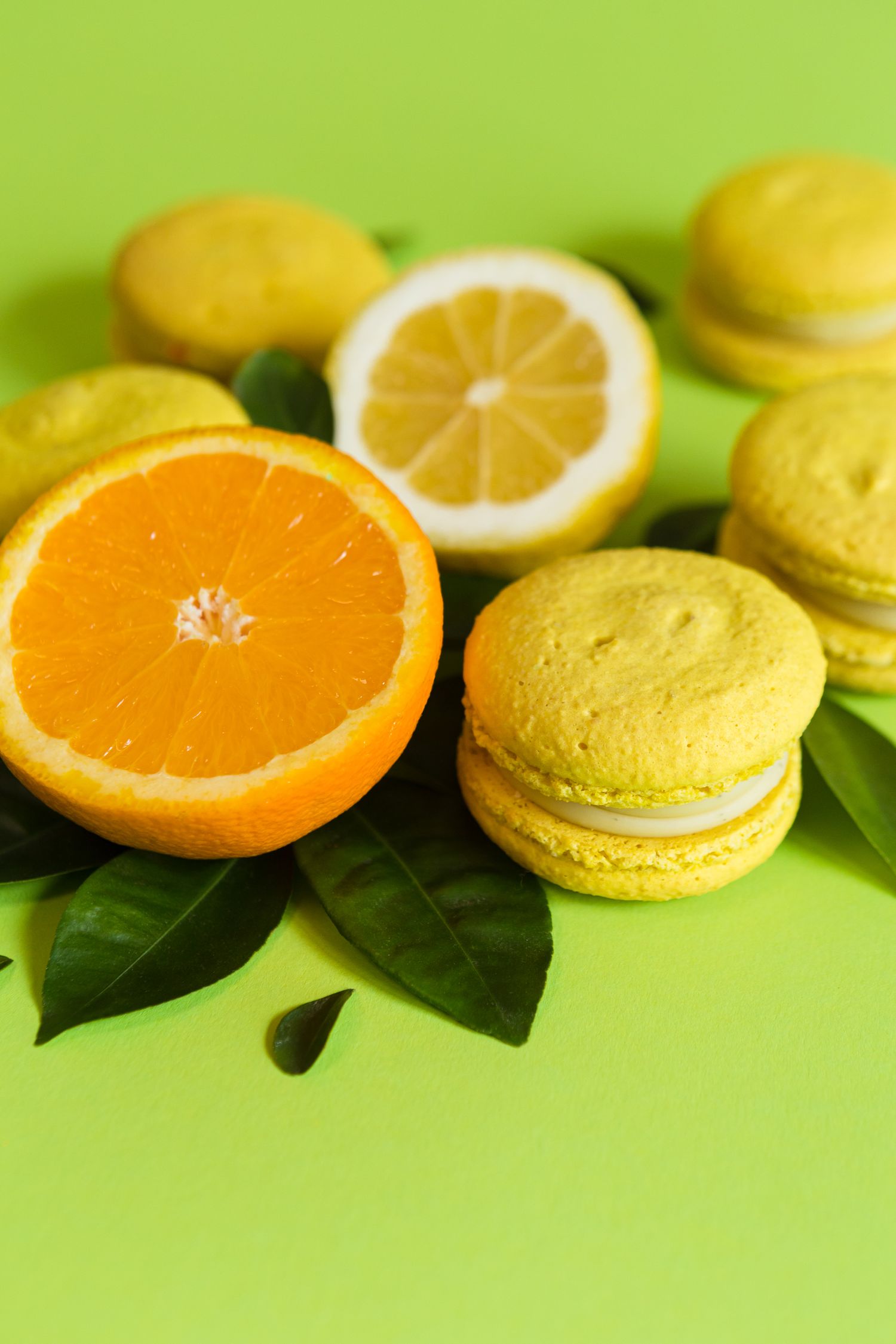 Yellow macarons with citrus slices and green leaves on bright lime background.