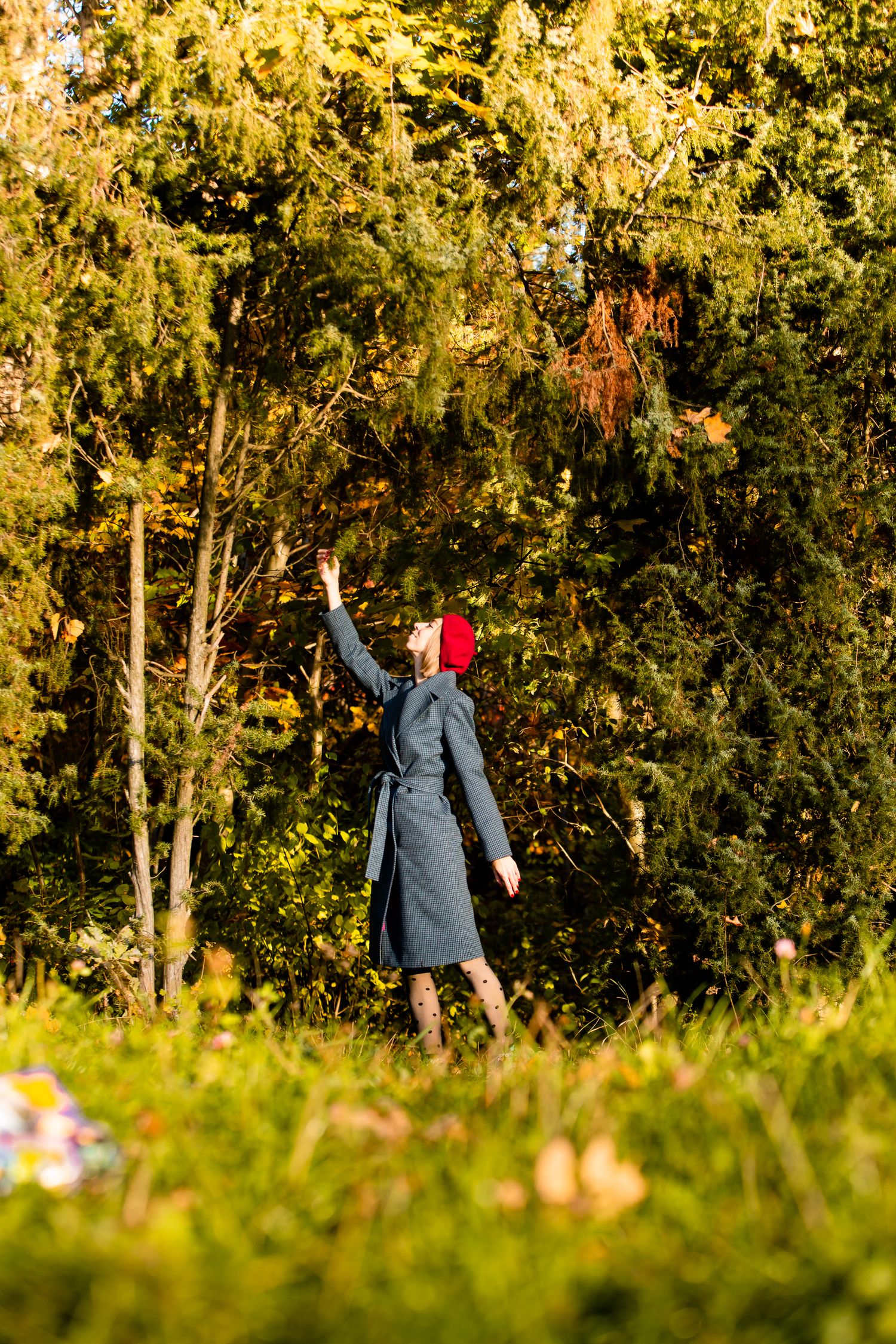 Figure in gray coat and red hat stretching arm upward against golden autumn trees.