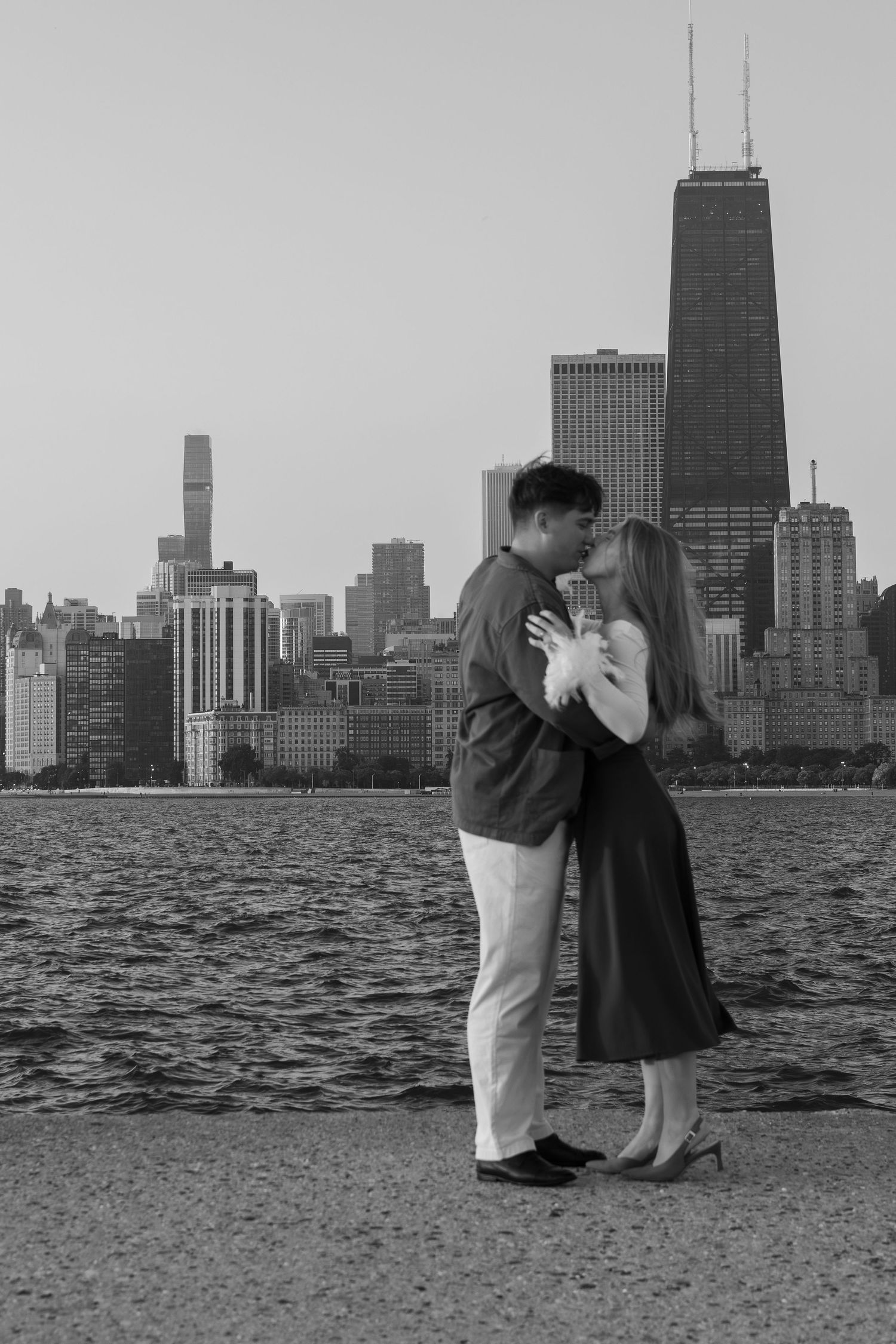 A couple embraces on the Chicago lakefront with the iconic skyline silhouetted in the background.