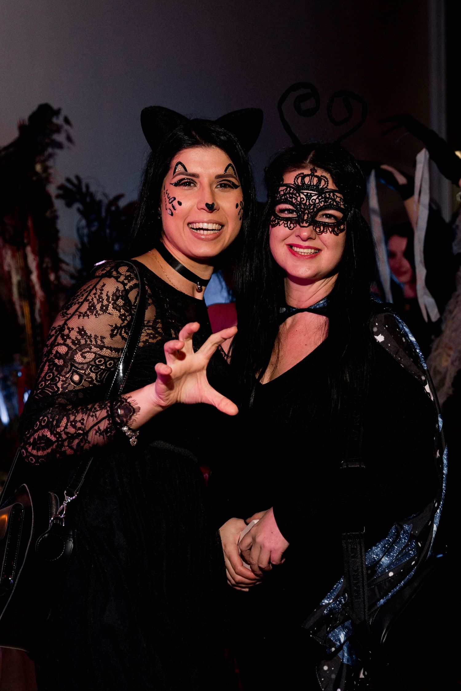 Two attendees at a costume party wearing cat ears and lace outfits pose together under dark lighting.