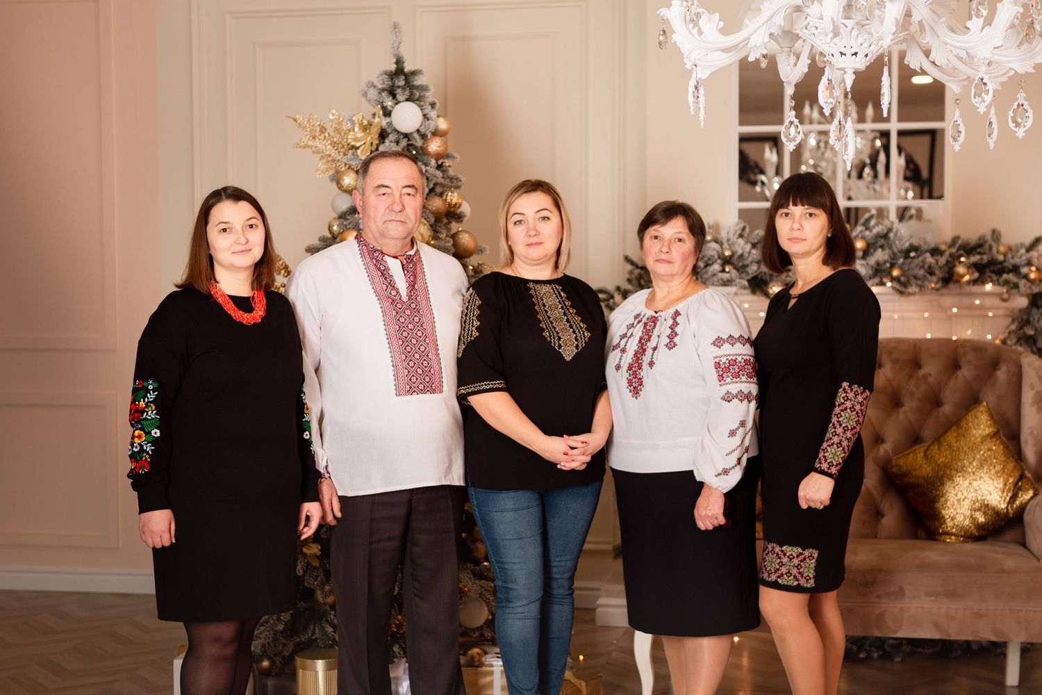 Group in formal attire with traditional embroidered details poses by holiday decorations.