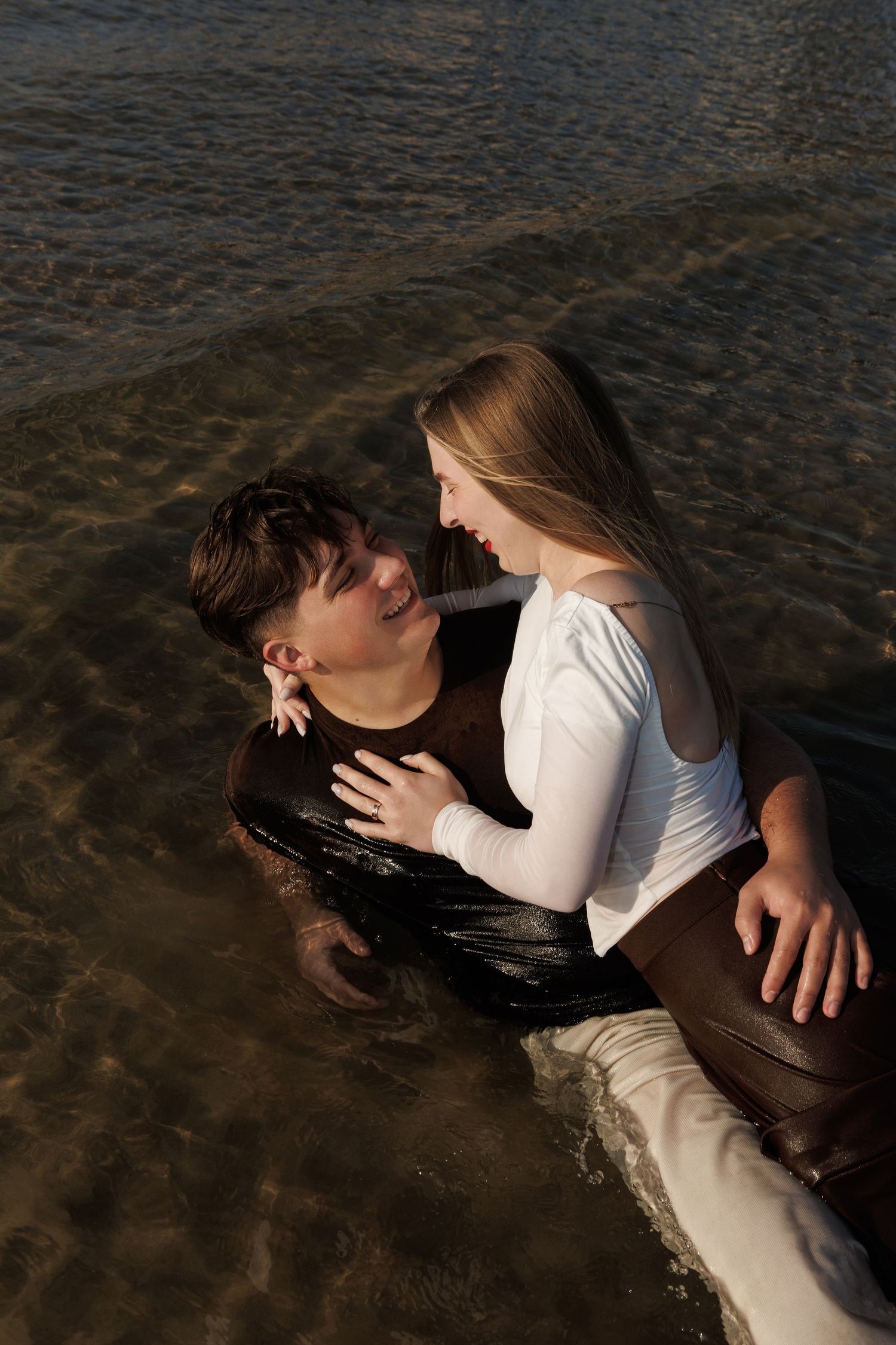 Two people in white clothing embrace near dark water creating a romantic artistic composition.