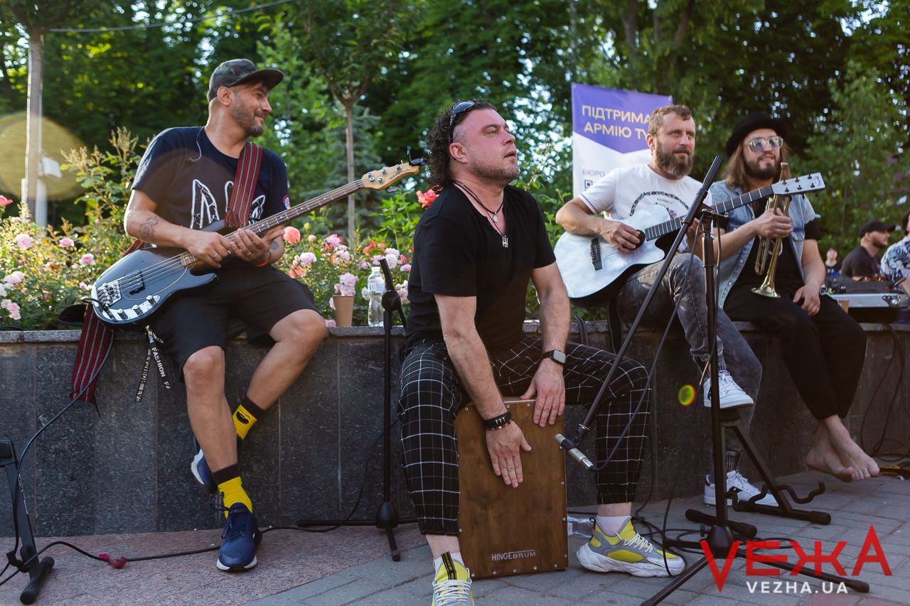 Band members performing on stage with acoustic guitars and percussion instruments.