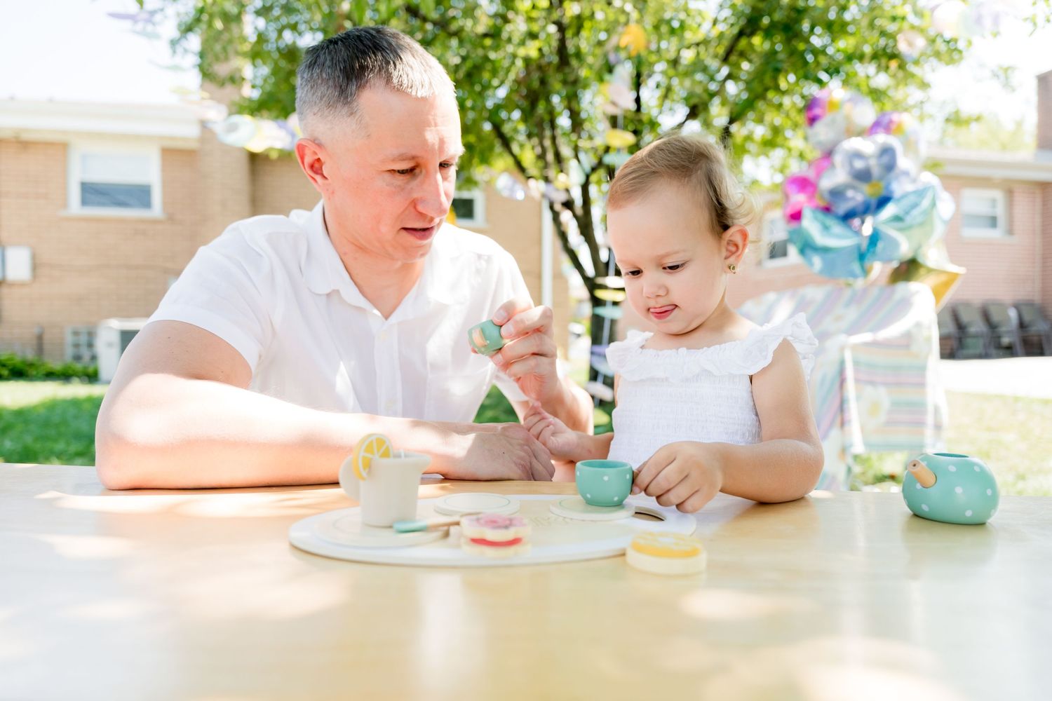 Two people enjoying tea and treats at an outdoor table on a sunny day.