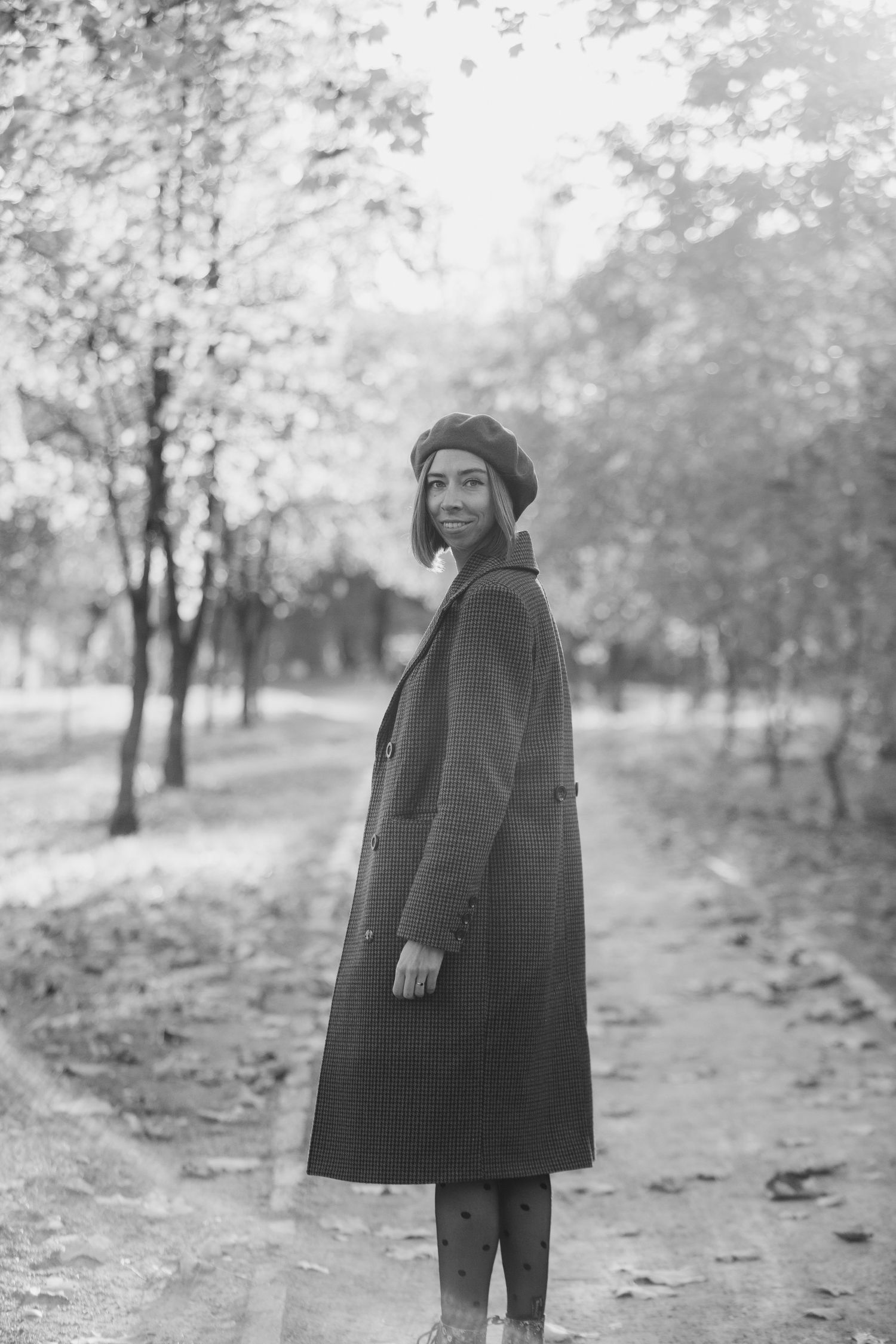 Black and white portrait on autumn path showing vintage-style coat and beret.