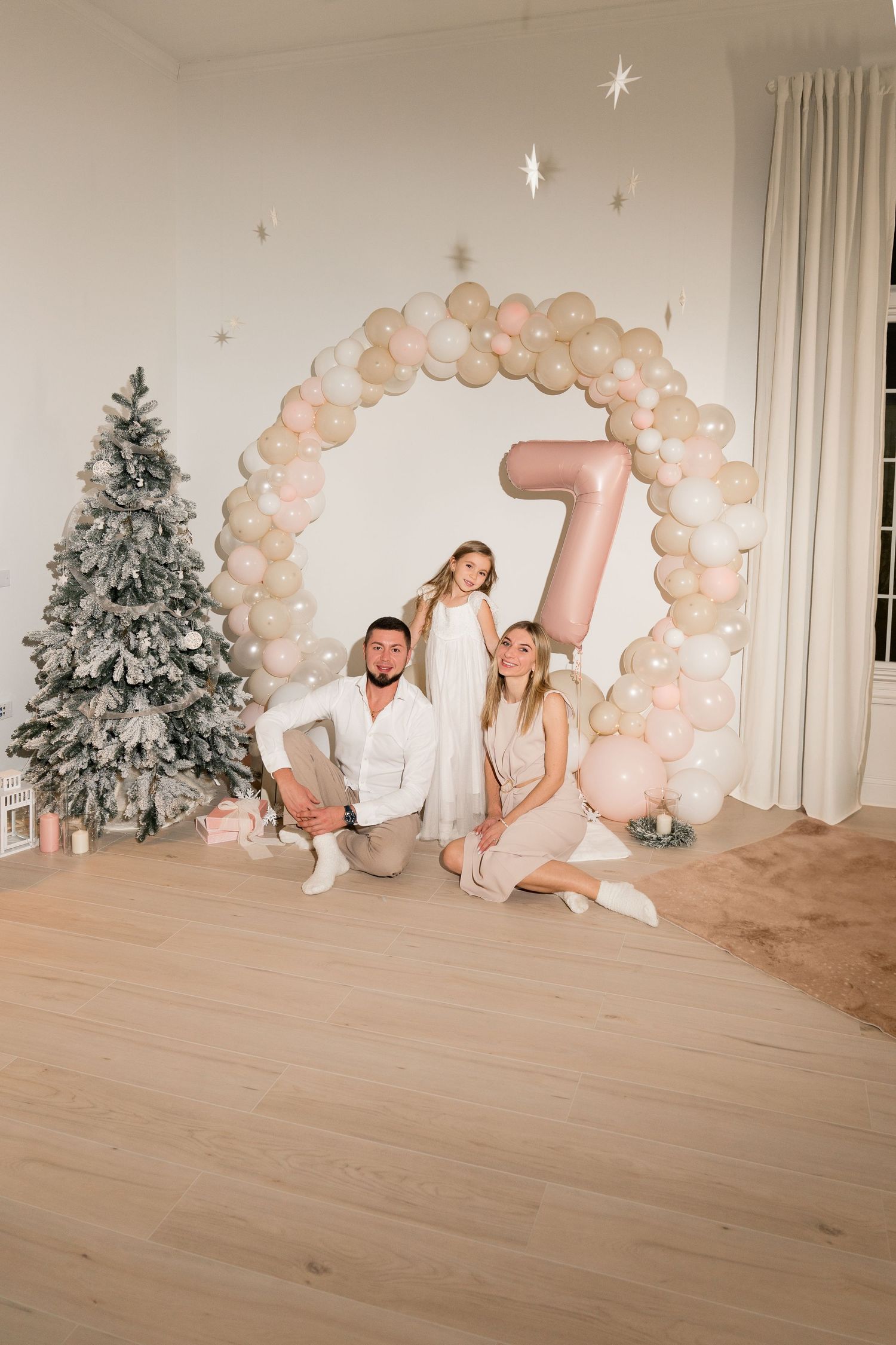 Christmas themed photo setup with balloon arch, flocked tree and number 7 decoration.