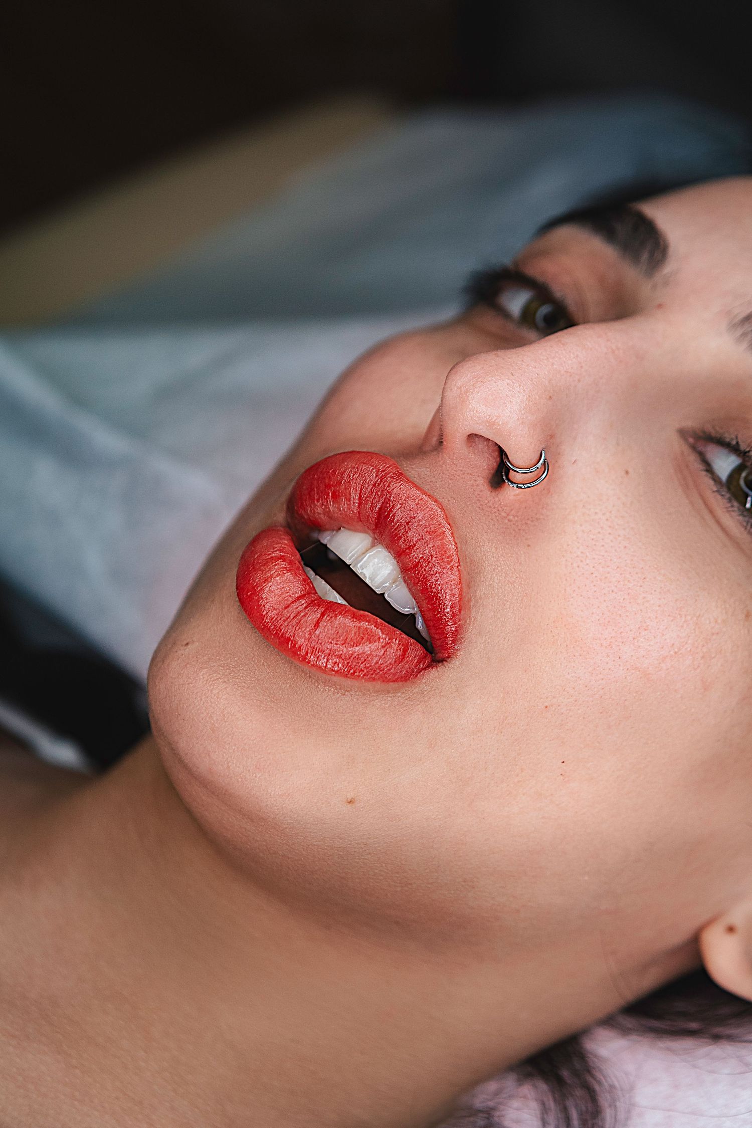 Close-up of red lips with septum piercing during a beauty procedure.