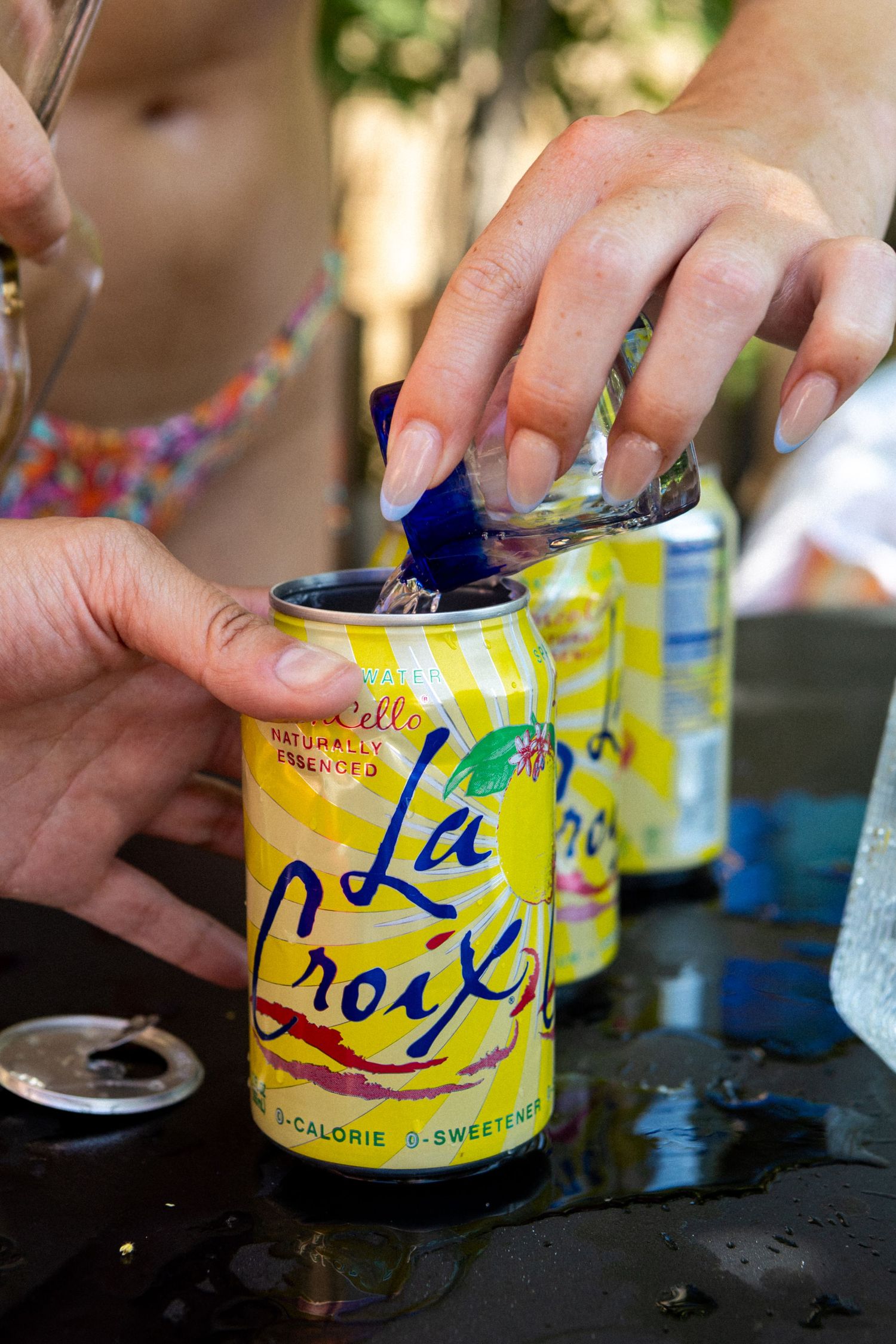 Someone opens a yellow can of La Croix sparkling water beverage on a dark surface at an outdoor gathering.