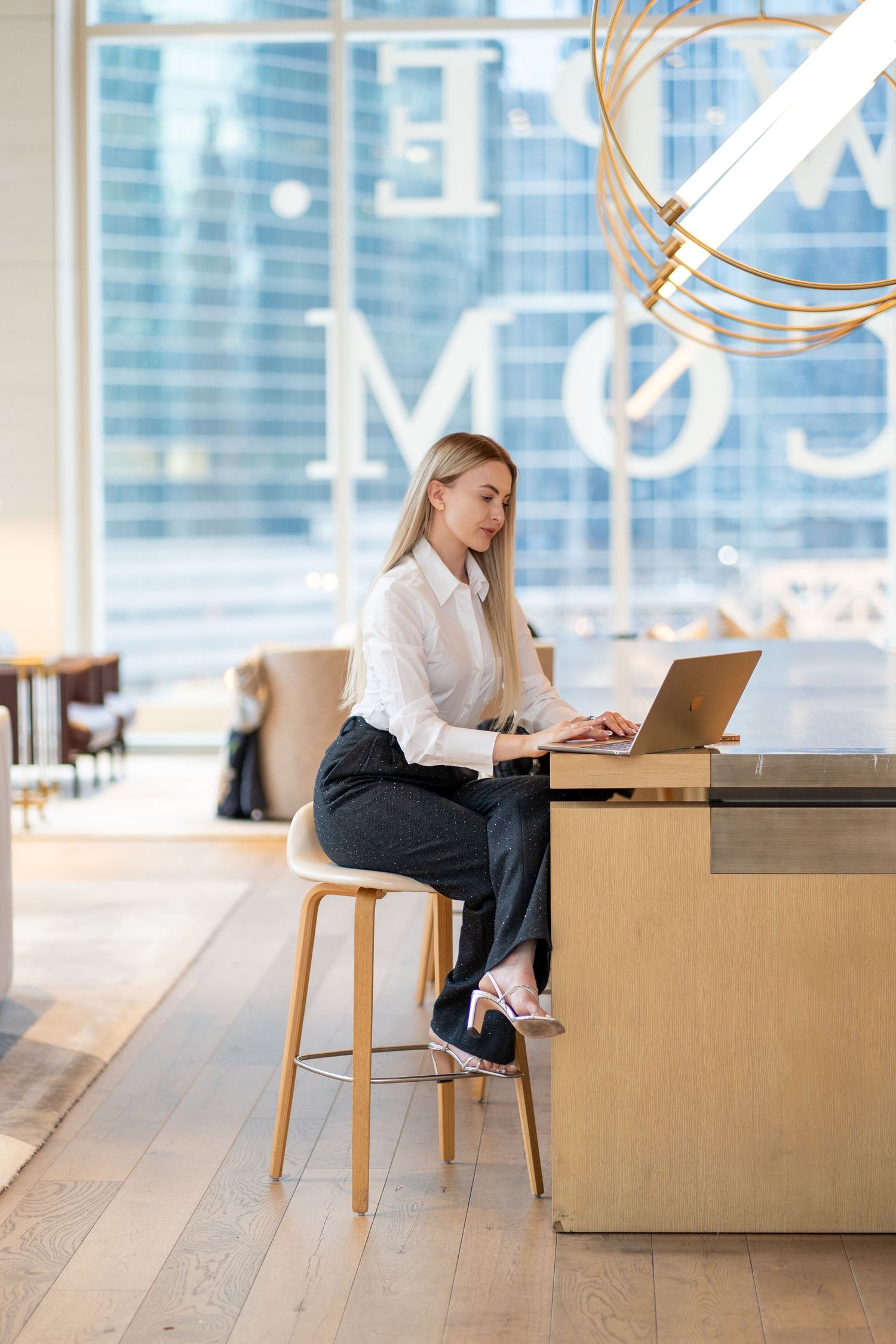 Business professional works on laptop at high counter in modern office setting.