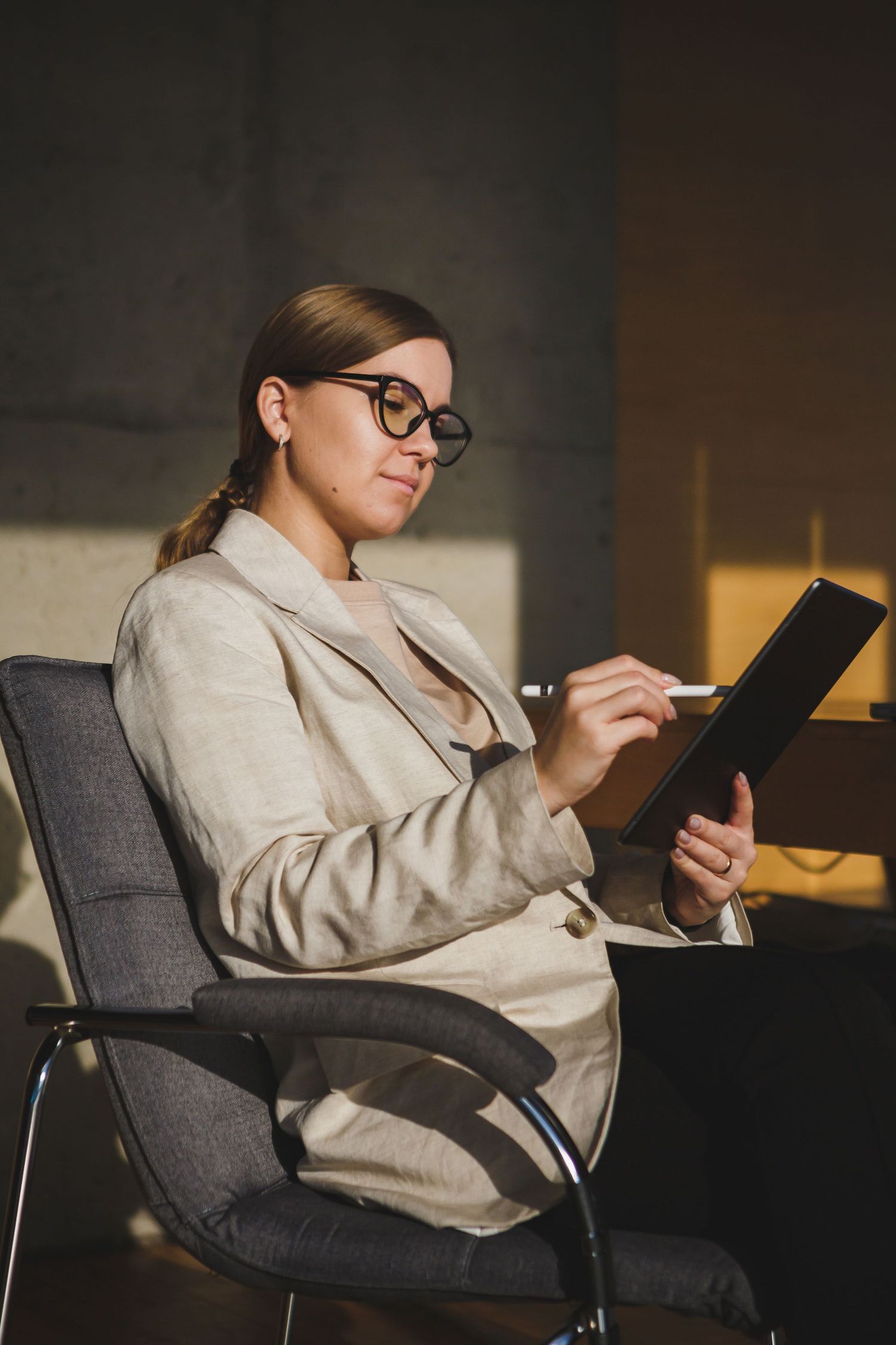 Professional in beige blazer working on tablet while seated in office chair.