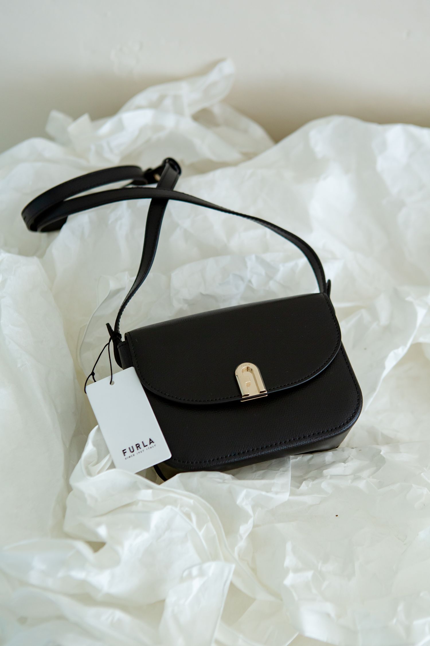 Black Furla handbag displayed on white crumpled paper background.