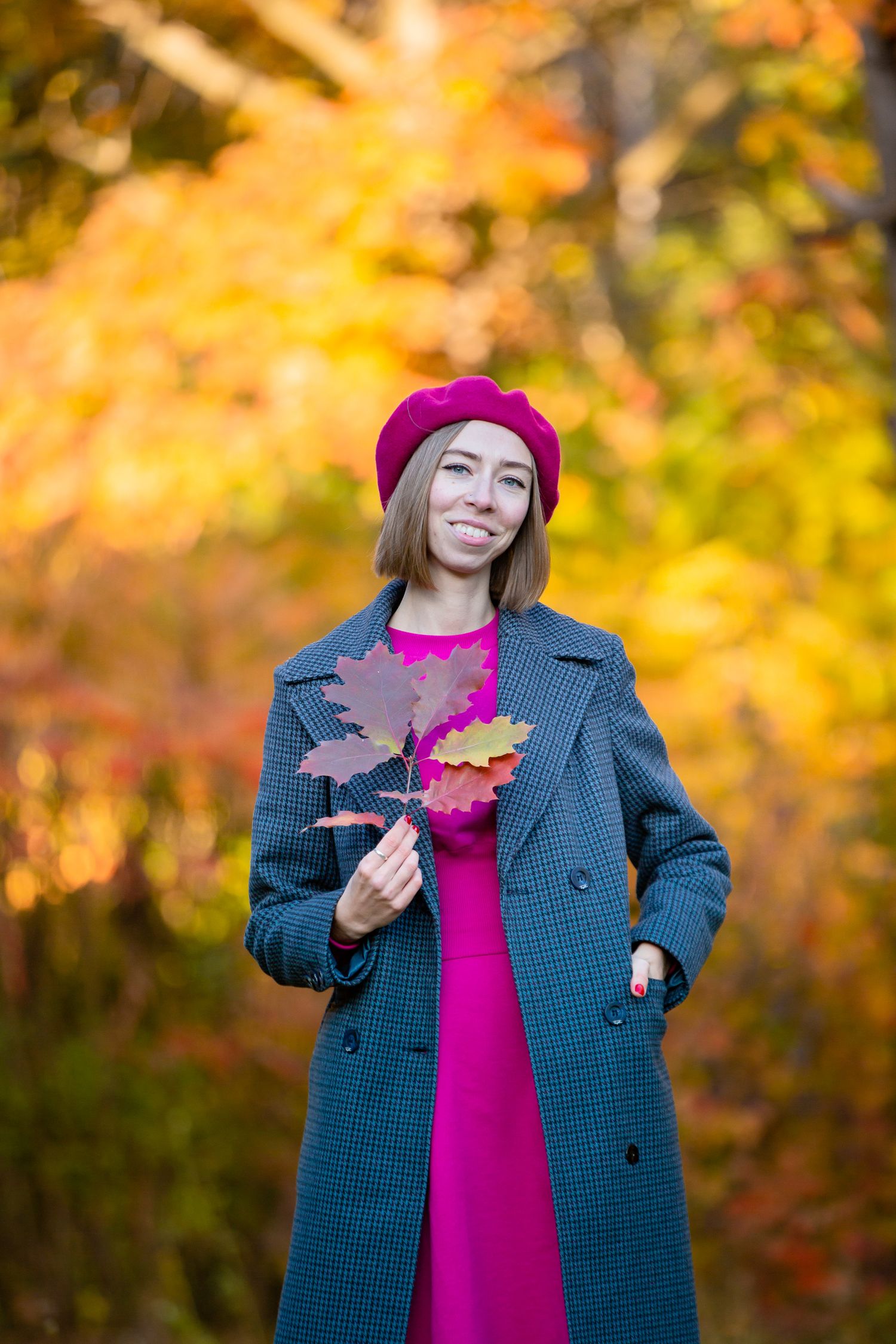 Autumn fashion portrait showing gray coat and burgundy beret with colorful fall leaves.