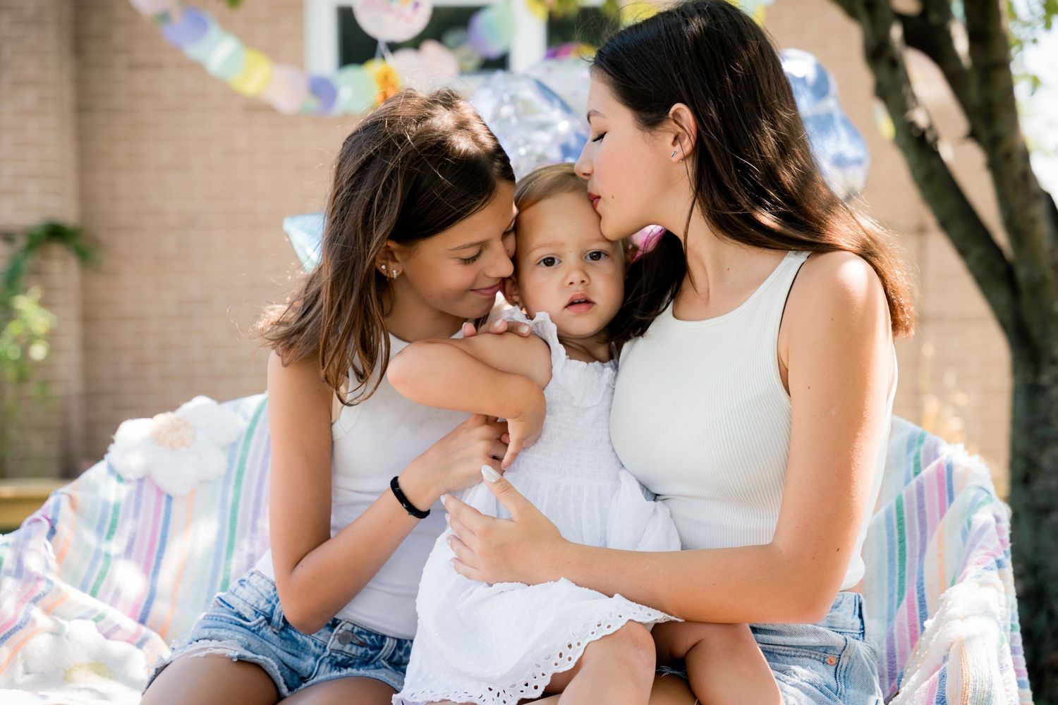 Three people share a tender moment together on a colorful blanket outdoors.