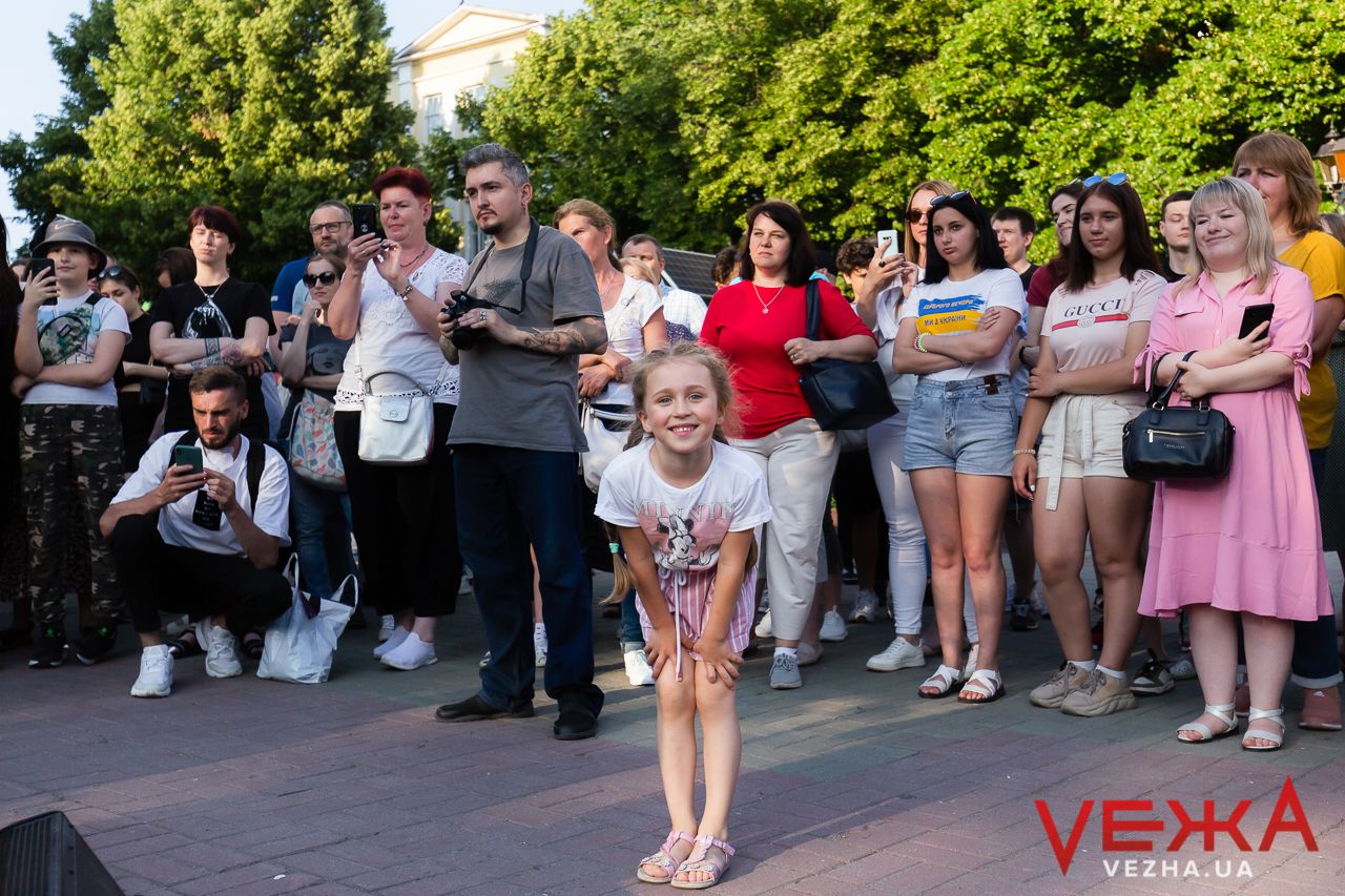 A crowd gathers to watch street performers in a sunny park setting.