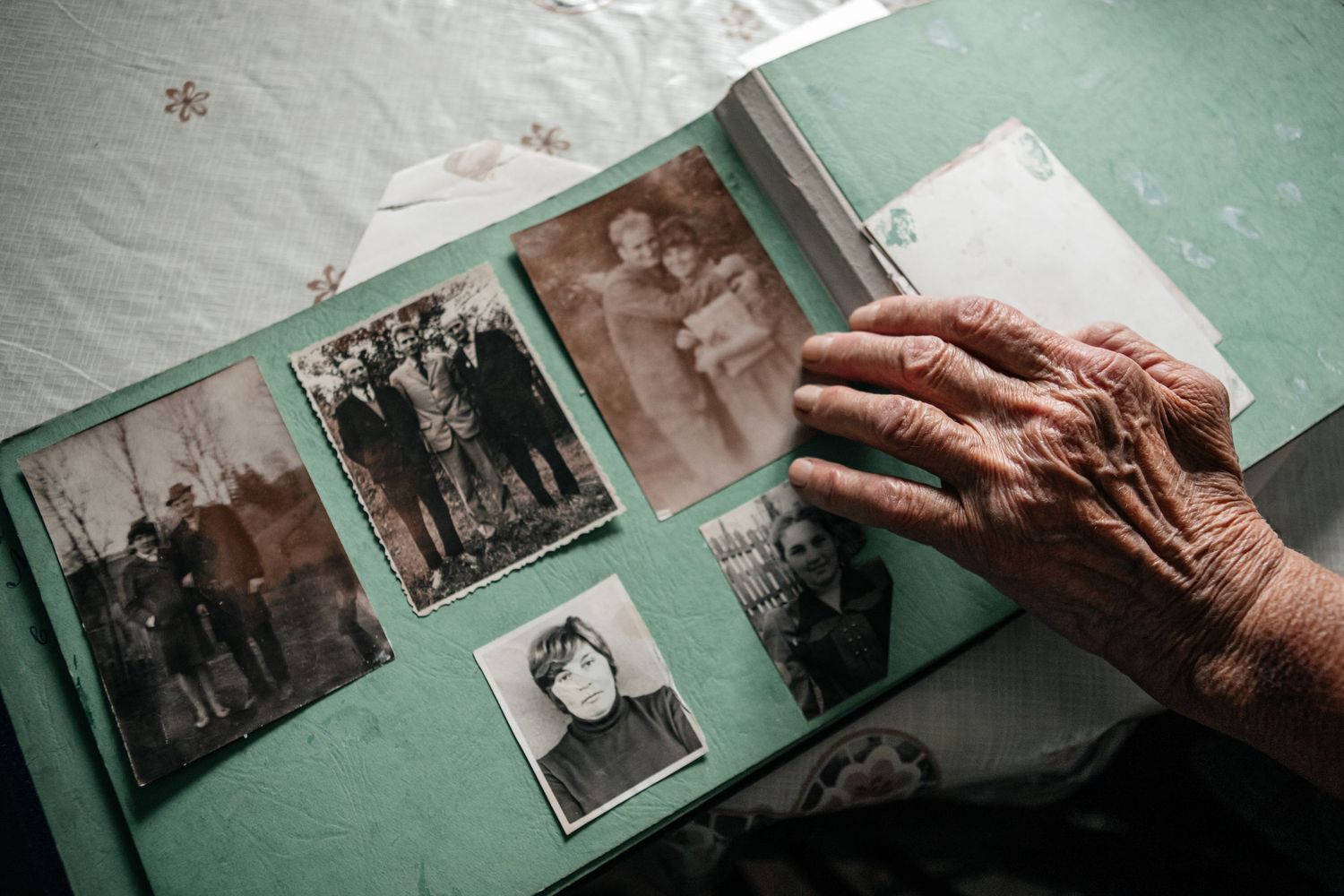 Weathered hand touches old photographs in a vintage photo album with mint green pages.